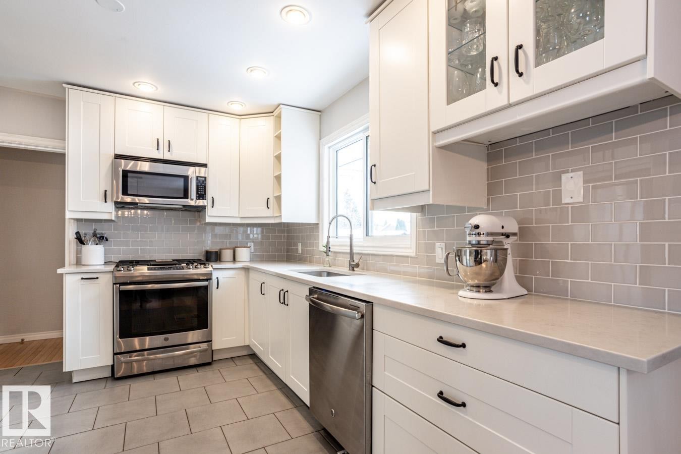 Well-appointed kitchen featuring white shaker-style cabinetry, stainless steel appliances, light-toned countertops, a subway tile backsplash, and recessed lighting - 8239 93A Avenue, Edmonton, AB - Indoor Photo Showing Kitchen With Stainless Steel Kitchen With Upgraded Kitchen