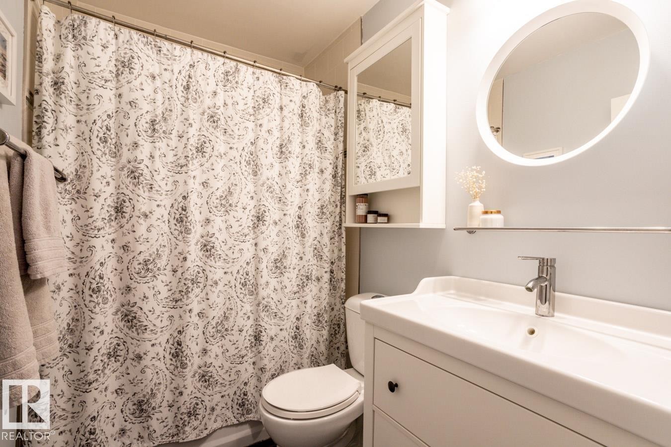 Bathroom featuring a white vanity with an integrated sink, a chrome faucet, and a round illuminated mirror - 8239 93A Avenue, Edmonton, AB - Indoor Photo Showing Bathroom