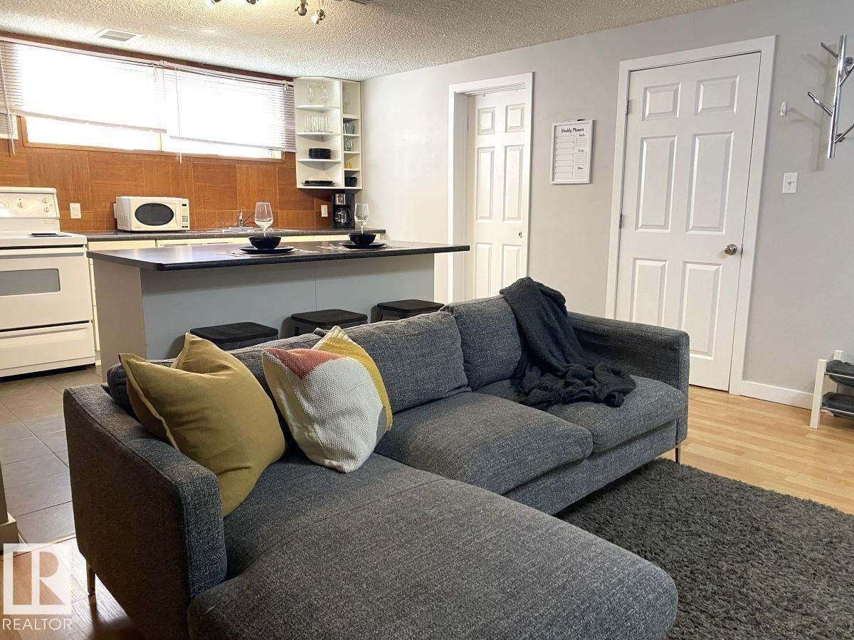 Open-concept living area featuring a kitchen island with seating, a white electric range, and a tiled backsplash - 8239 93A Avenue, Edmonton, AB - Indoor