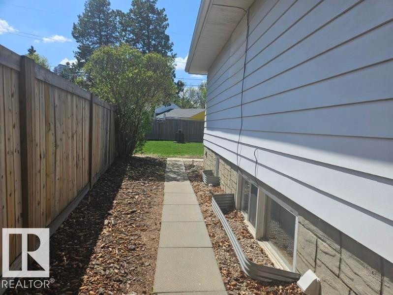 Side yard access featuring a concrete pathway, a wood privacy fence, and a planting bed with wood chip ground cover - 8239 93A Avenue, Edmonton, AB - Outdoor With Exterior