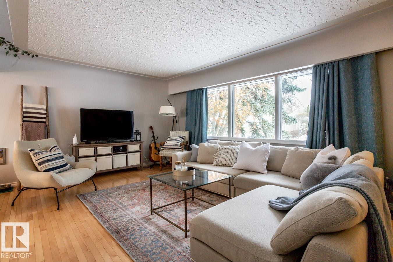 Spacious living area featuring light wood-finish flooring, ample natural light from multiple windows, and a neutral color palette - 8239 93A Avenue, Edmonton, AB - Indoor Photo Showing Living Room