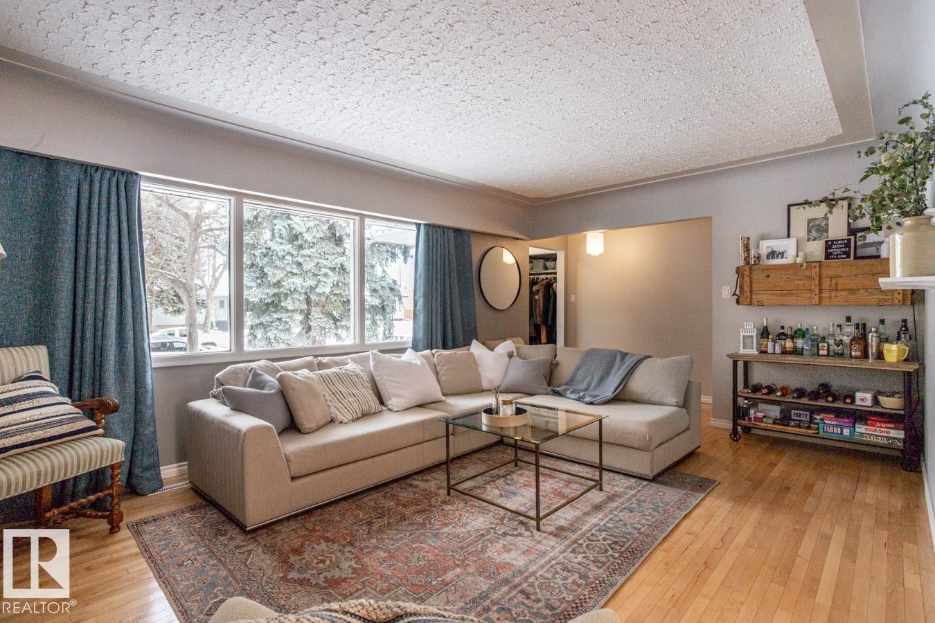 Living space with wood-finish flooring, a large window array, and a neutral wall color - 8239 93A Avenue, Edmonton, AB - Indoor Photo Showing Living Room