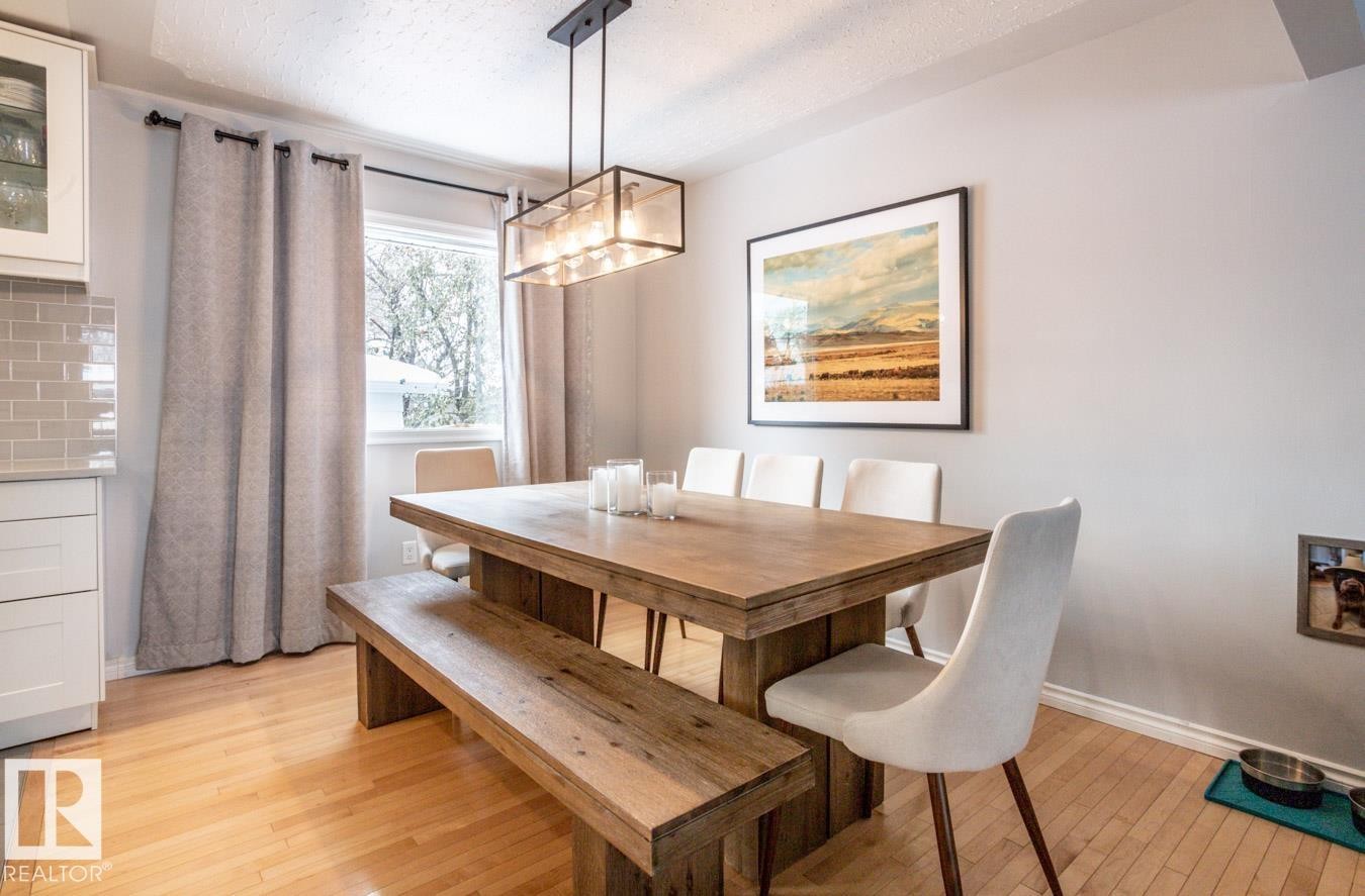 Dining area featuring wood-finish flooring, a rectangular window with white trim, and a linear pendant light fixture - 8239 93A Avenue, Edmonton, AB - Indoor Photo Showing Dining Room