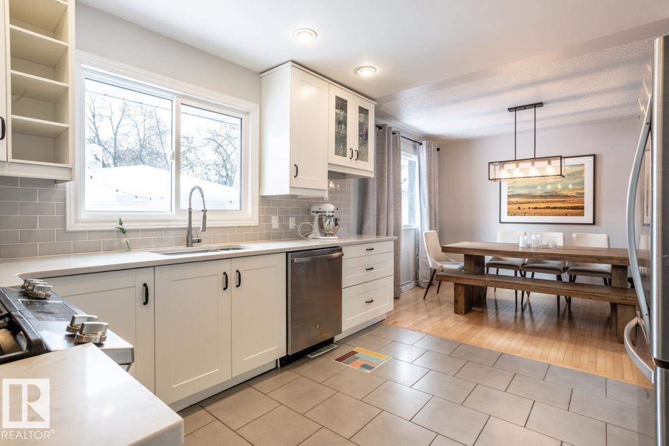 Kitchen featuring white shaker cabinetry, light-toned countertops, a stainless steel sink with a gooseneck faucet, and a grey subway tile backsplash - 8239 93A Avenue, Edmonton, AB - Indoor