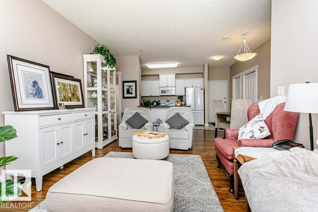 Open-concept living area with wood-finish flooring, white built-in cabinetry, and integrated kitchen space - 323 16807 100 Avenue, Edmonton, AB - Indoor Photo Showing Living Room