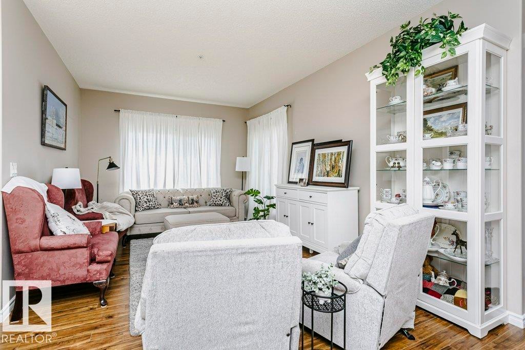 Living area featuring wood-finish flooring, neutral wall tones, and white window treatments - 323 16807 100 Avenue, Edmonton, AB - Indoor Photo Showing Living Room