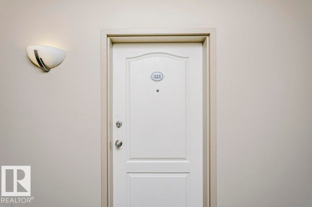 White paneled entry door with polished chrome hardware and an overhead wall sconce - 323 16807 100 Avenue, Edmonton, AB - Photo Showing Other Room