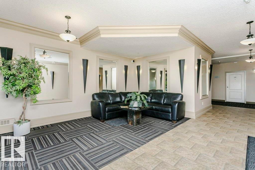 Lobby area featuring mixed-patterned flooring, wall-mounted mirrors, decorative sconces, and crown molding accents - 323 16807 100 Avenue, Edmonton, AB - Indoor