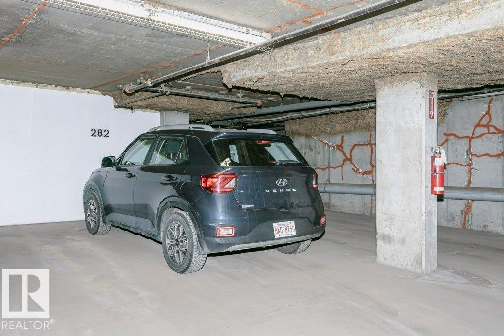 Designated parking space with concrete flooring, exposed overhead piping, concrete support pillar, and fire safety equipment - 323 16807 100 Avenue, Edmonton, AB - Indoor Photo Showing Garage