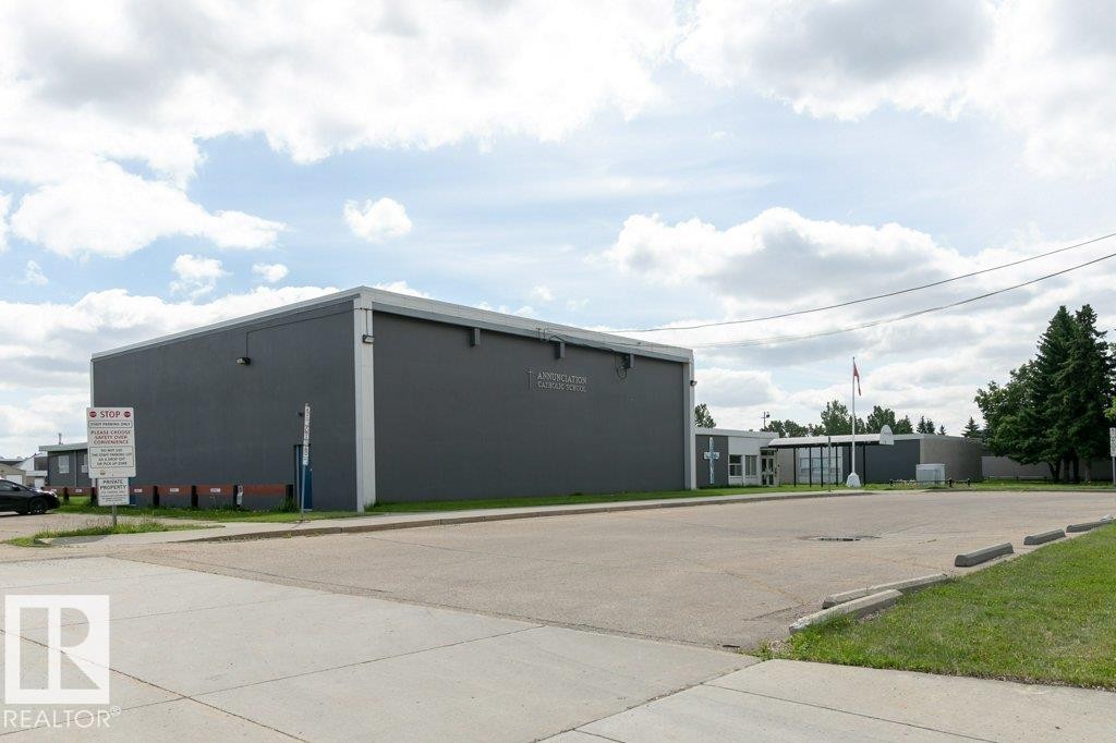 Expansive paved parking lot with multiple parking spaces and curbing, fronting a large commercial-style building with a dark gray facade and a flat roof - 323 16807 100 Avenue, Edmonton, AB - Outdoor
