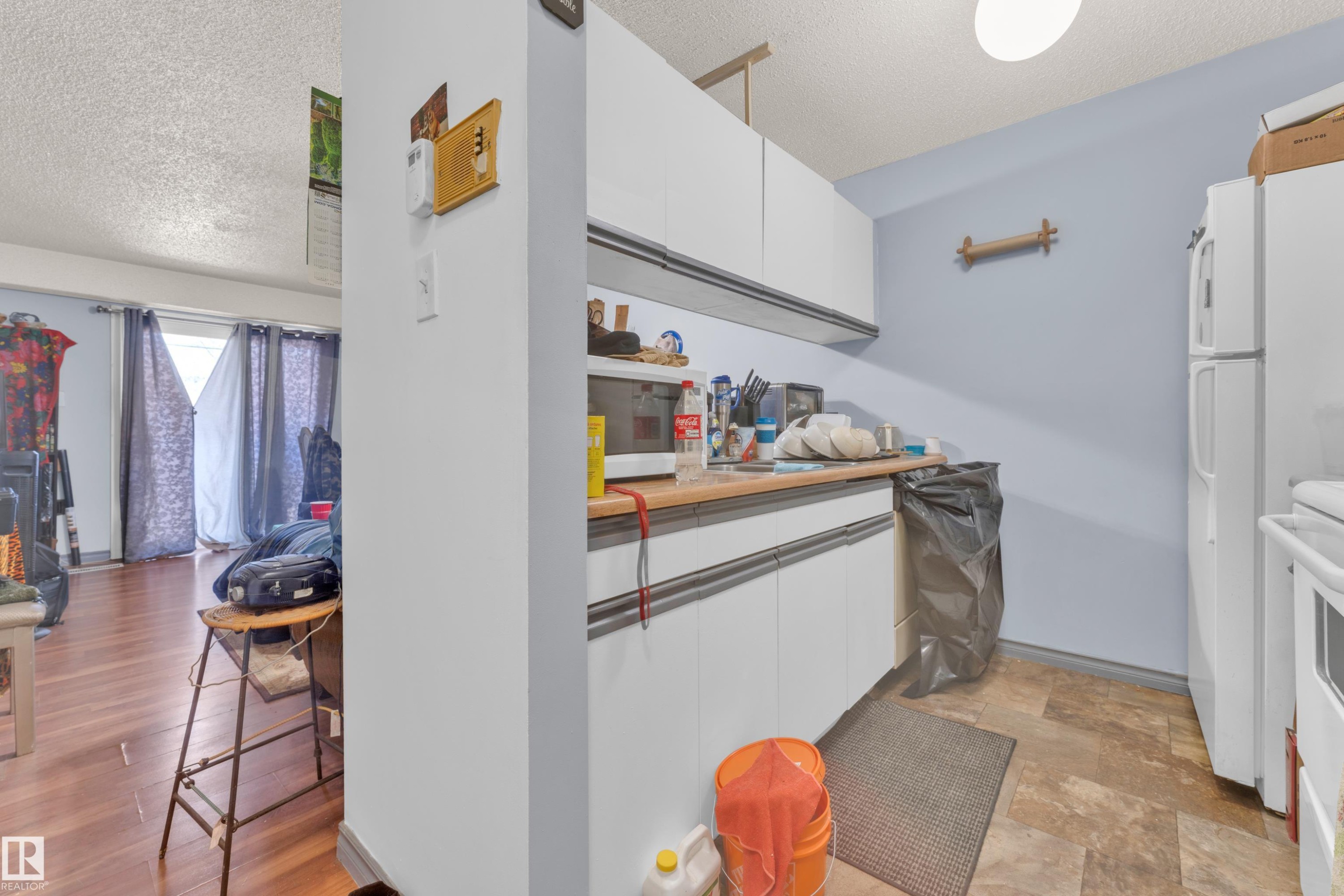Compact kitchen area featuring white upper and lower cabinetry, a light-toned countertop, and patterned floor tiling - 101 10136 160 Street Nw, Edmonton, AB - Indoor Photo Showing Other Room