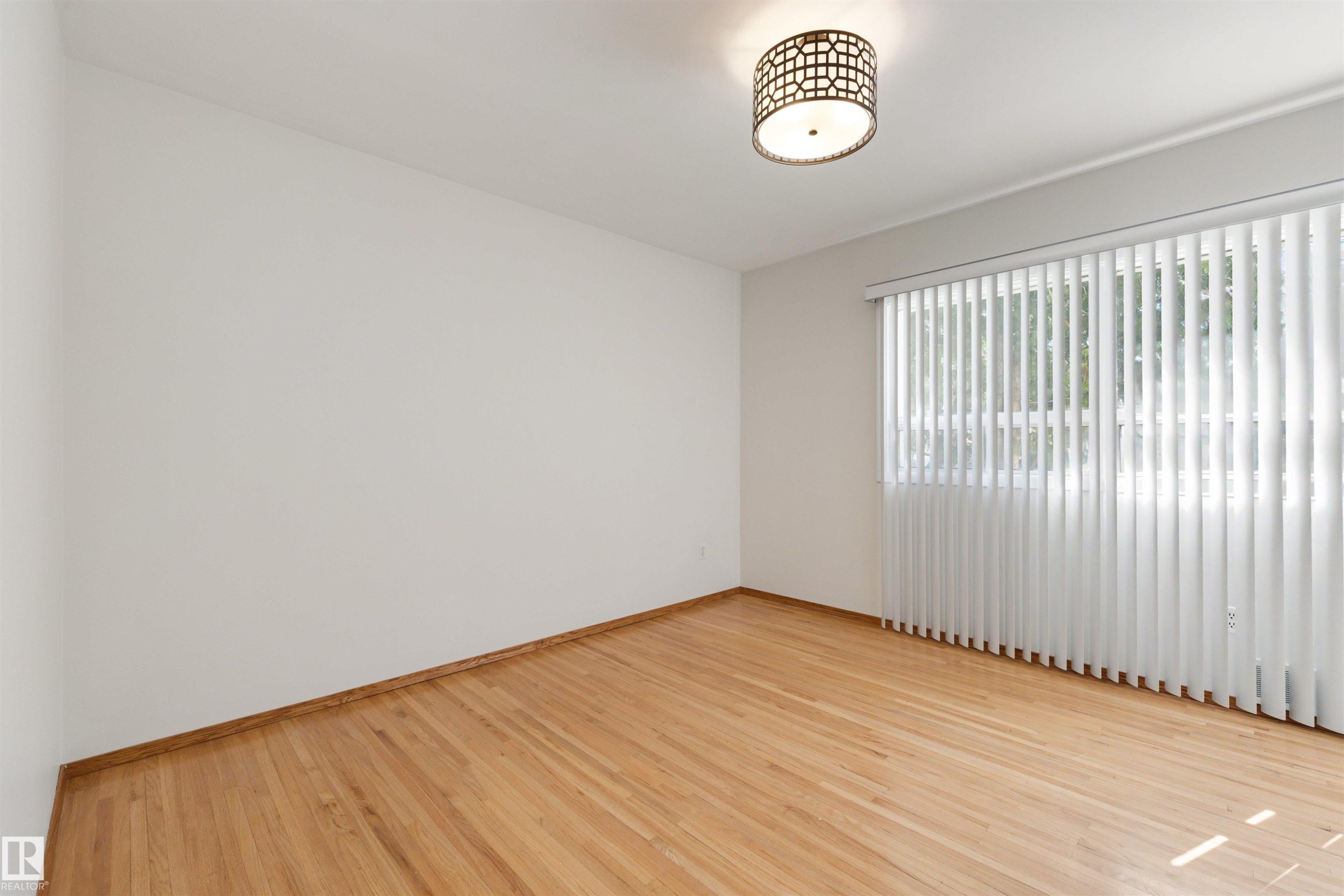 Room featuring wood-finish flooring, white walls, and a window with vertical blinds - 9602 85 Street, Edmonton, AB