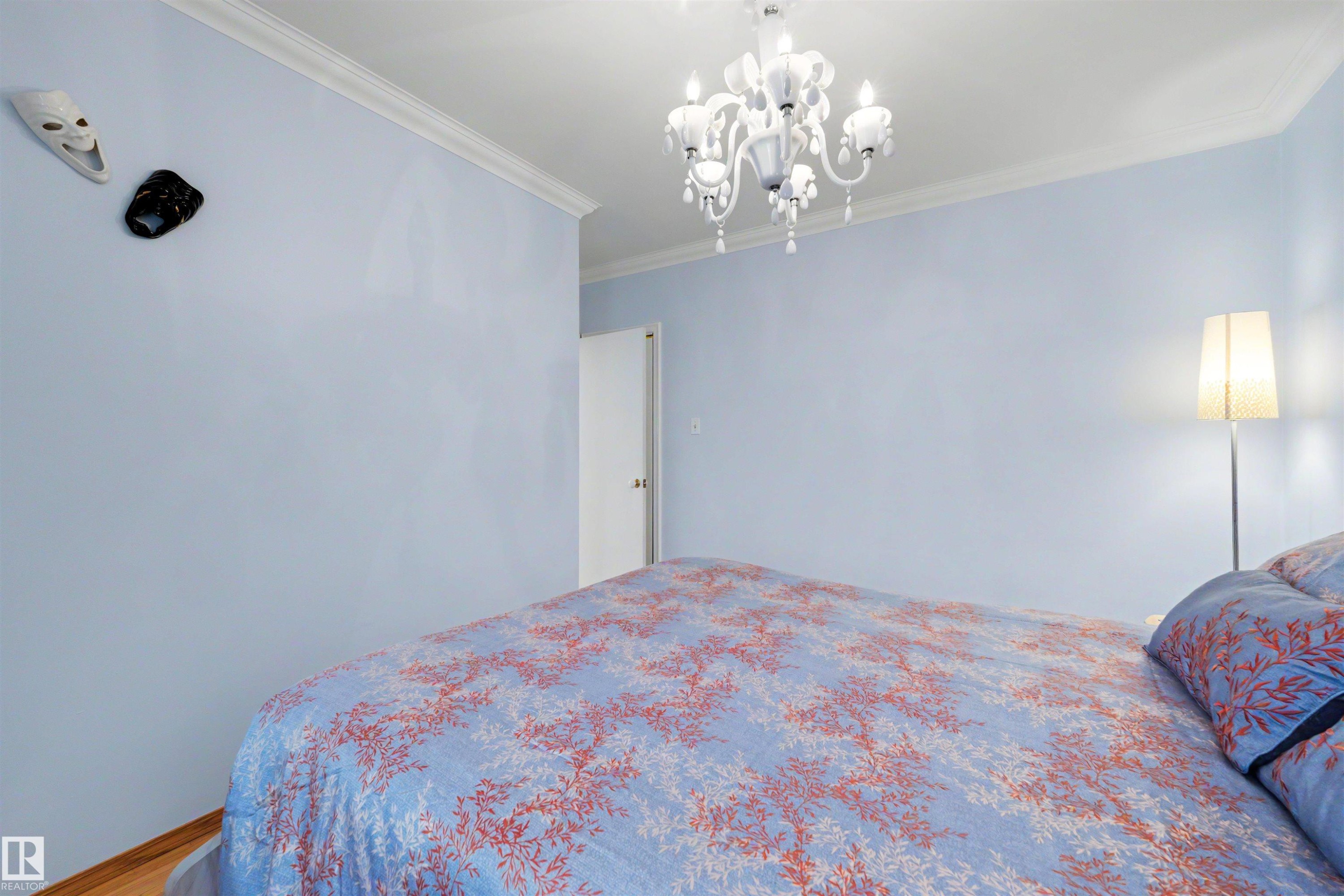 Spacious interior room featuring light blue walls, a white chandelier, crown molding, and wood-finish flooring - 9602 85 Street, Edmonton, AB