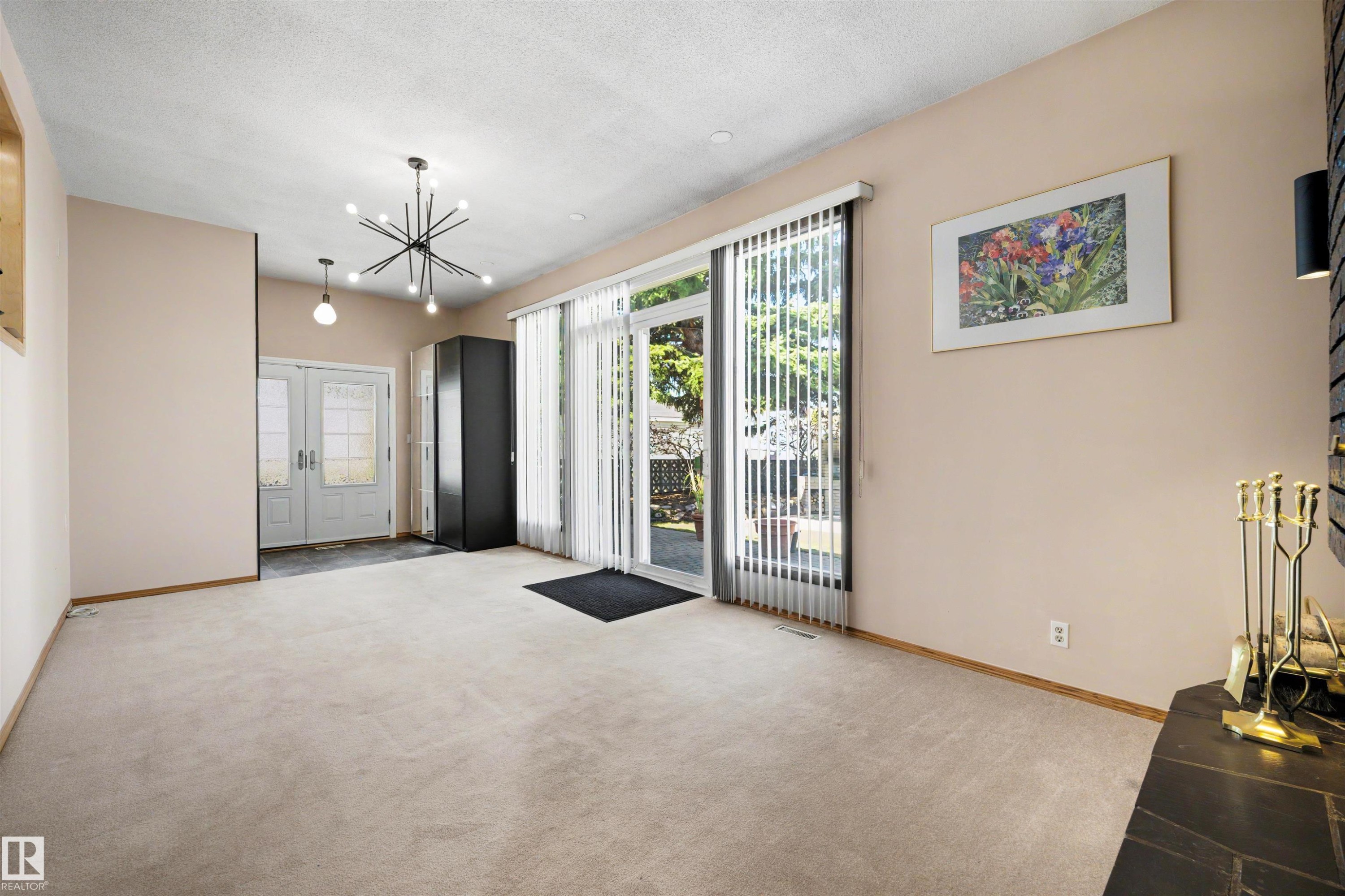 Carpeted living area featuring a modern sputnik chandelier, double entry doors, and a glass sliding door with vertical blinds - 9602 85 Street, Edmonton, AB
