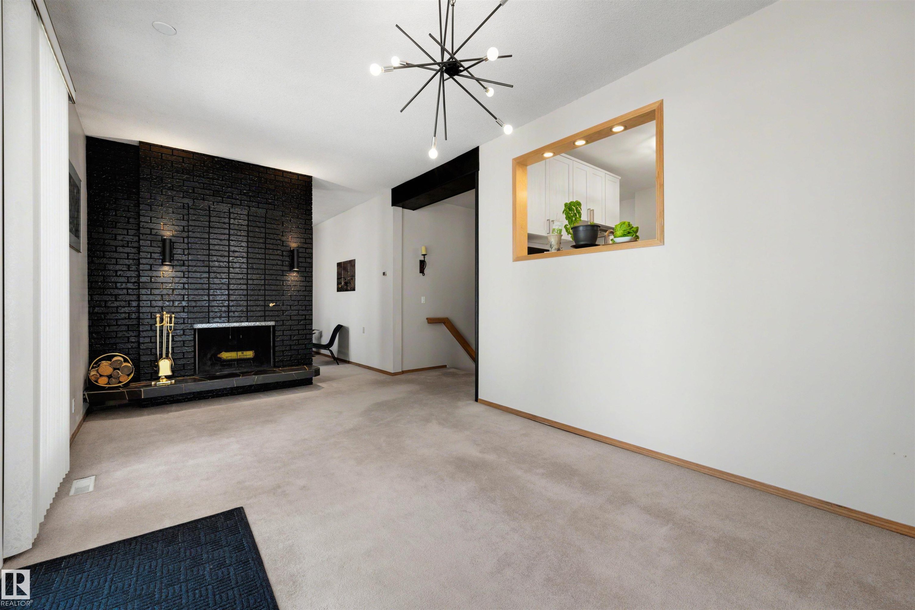 Living area featuring a black brick fireplace with a raised hearth, light carpet flooring, and a pass-through window with wood trim - 9602 85 Street, Edmonton, AB