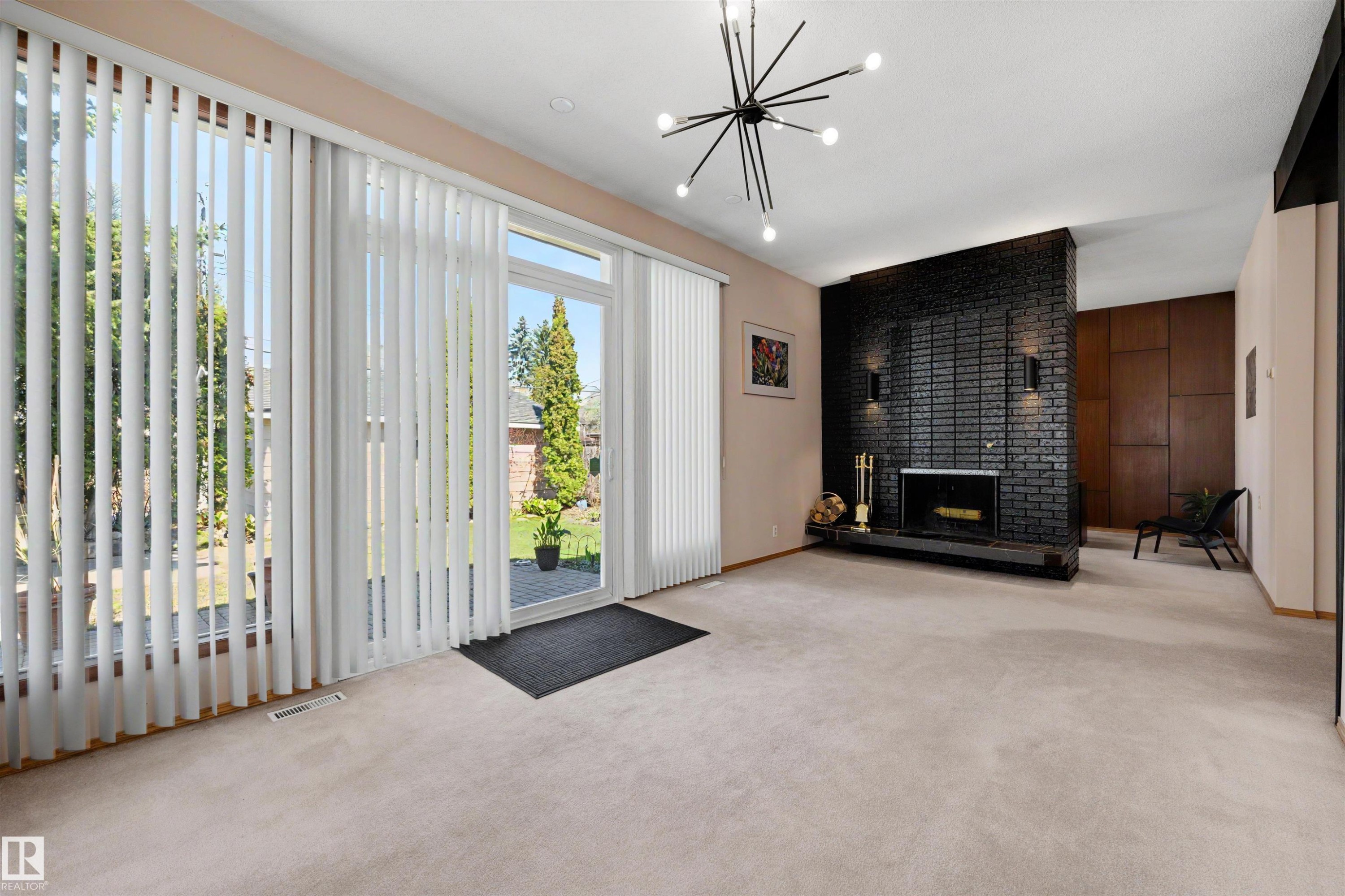Living area featuring a black brick fireplace with a hearth, carpeted flooring, and a modern chandelier - 9602 85 Street, Edmonton, AB