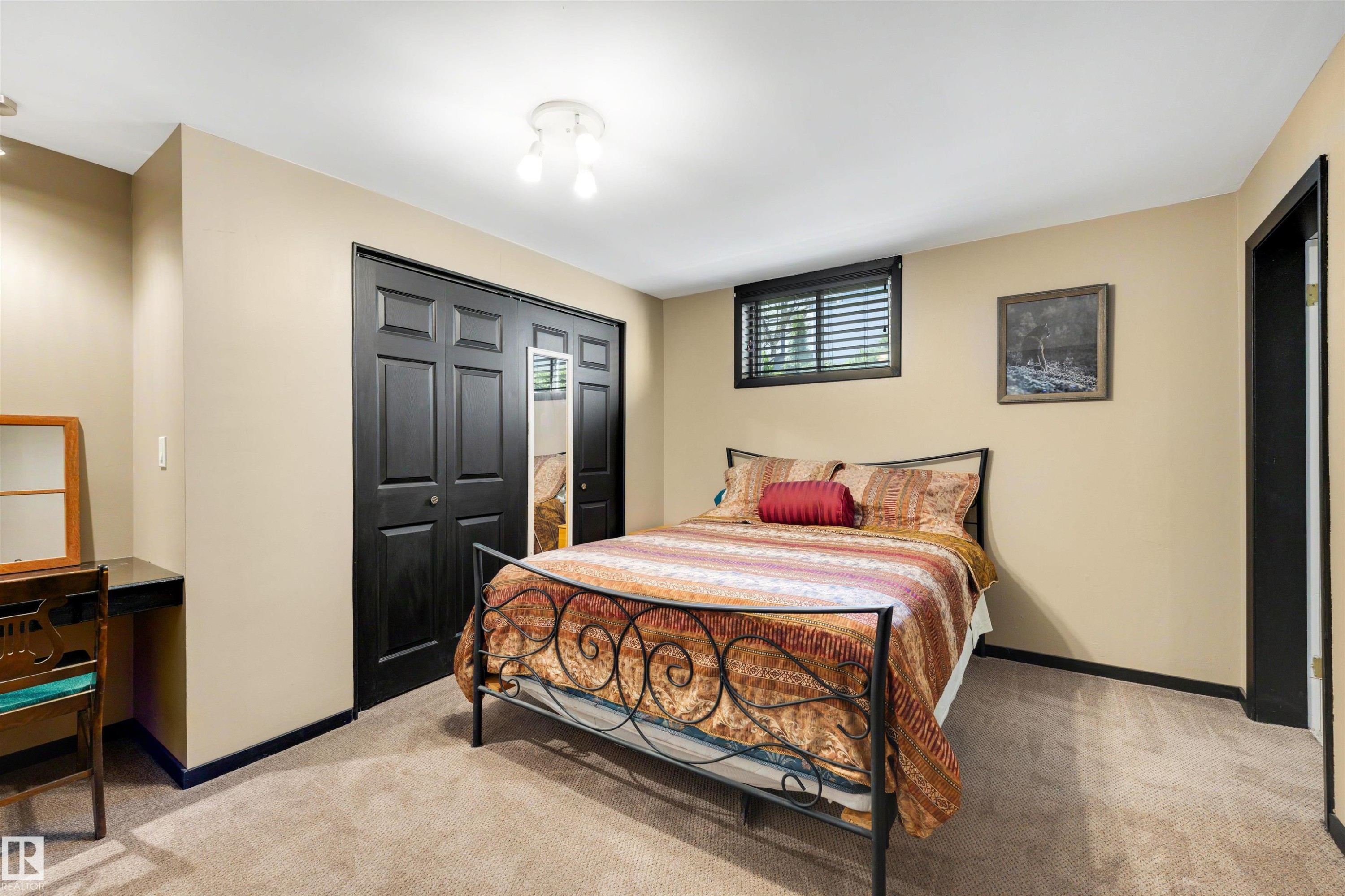Carpeted room featuring a window with horizontal blinds, black bi-fold closet doors, a built-in desk area, and recessed lighting - 9602 85 Street, Edmonton, AB