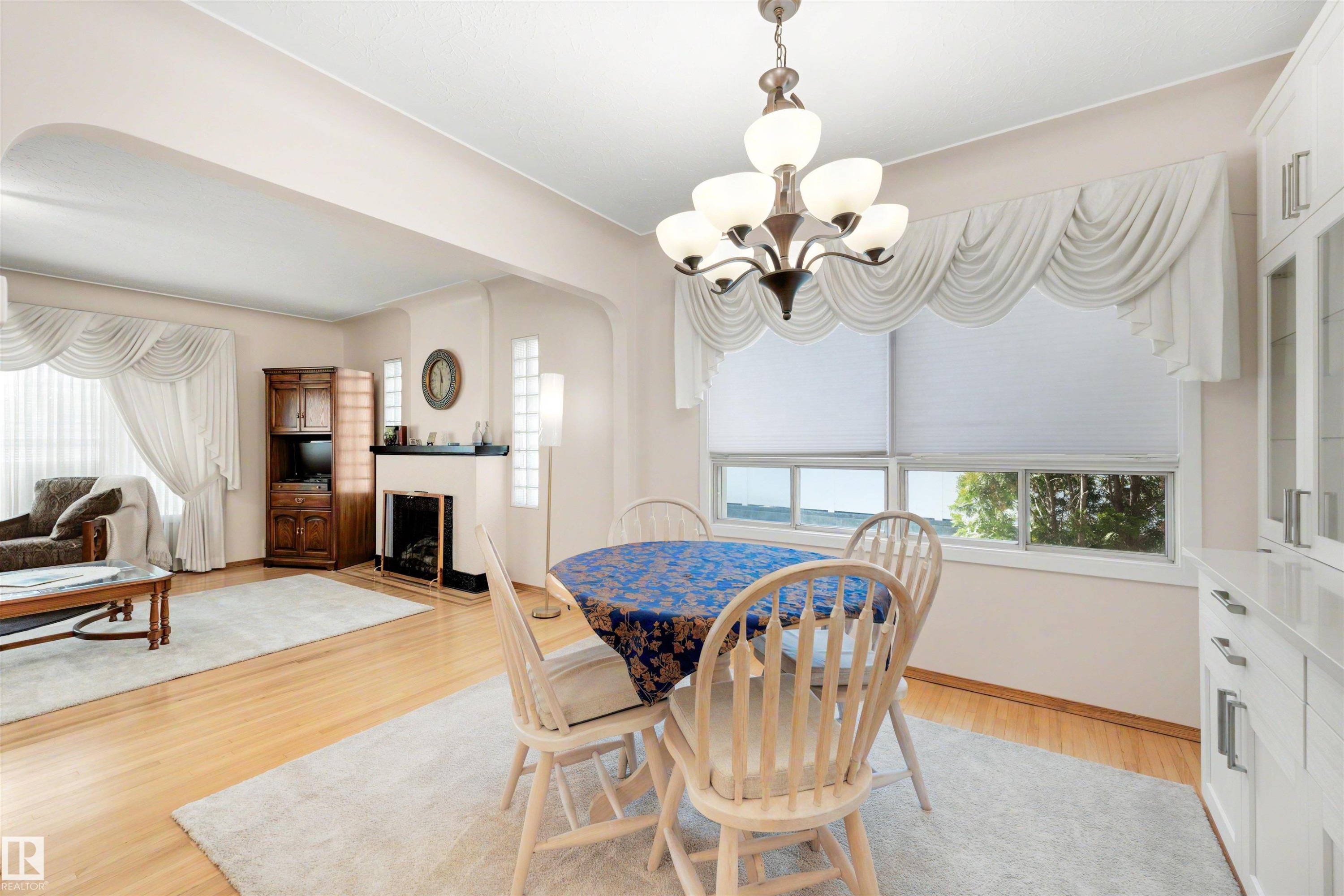Dining area featuring a multi-bulb chandelier, a large window with roller shades, and light wood-finish flooring - 9602 85 Street, Edmonton, AB