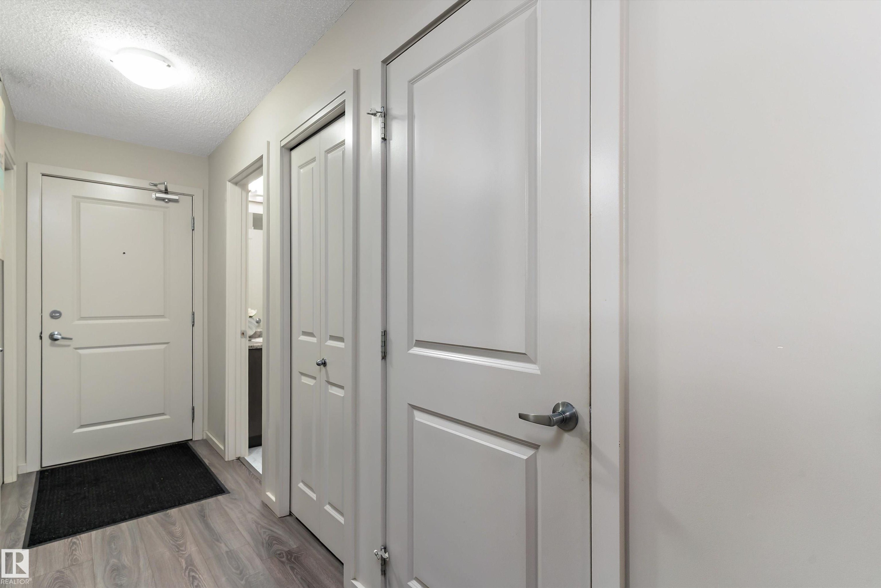 Entryway featuring wood-finish flooring, light neutral paint, and white paneled doors - 231 344 Windermere Road, Edmonton, AB - Indoor Photo Showing Other Room