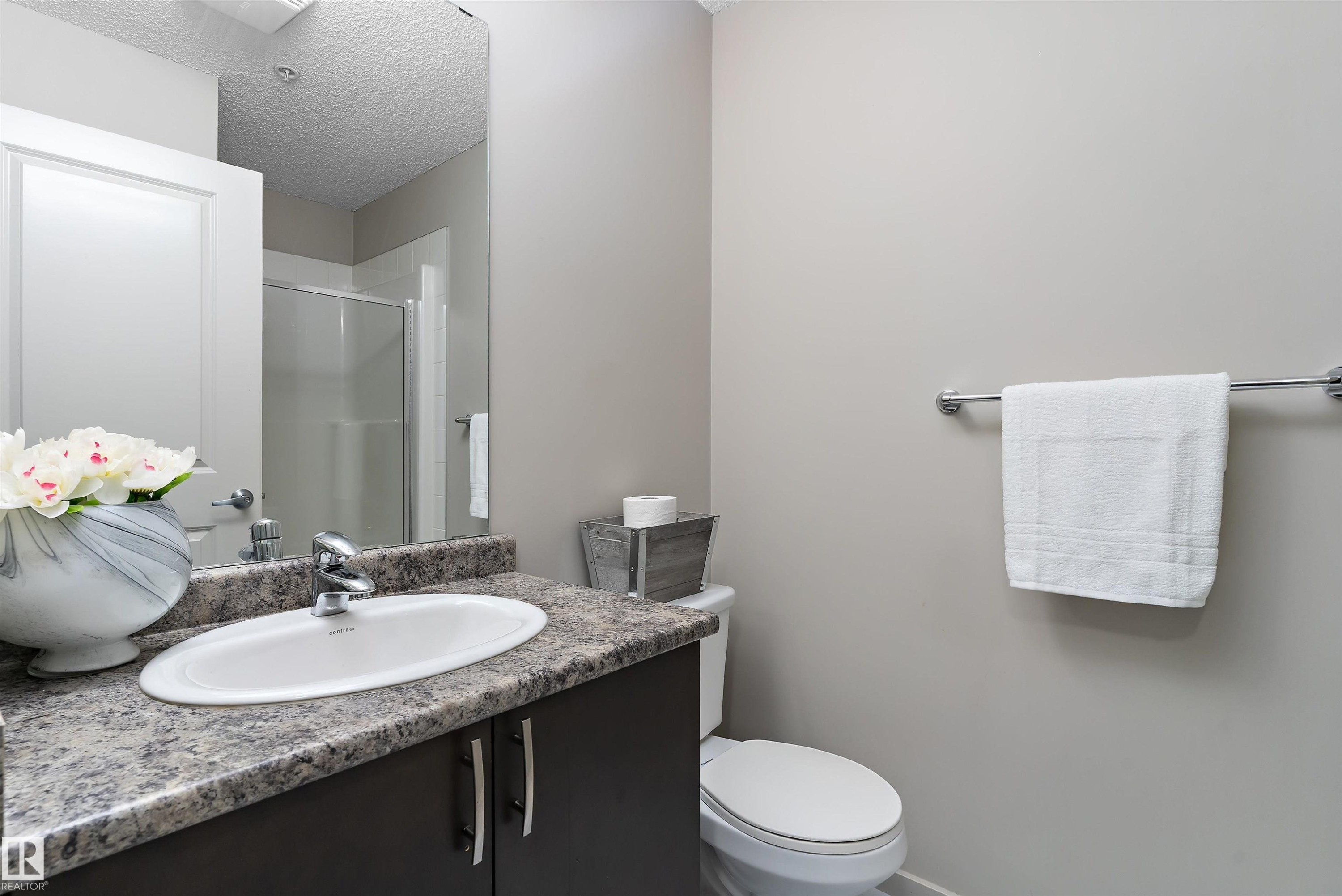 Bathroom vanity featuring a rectangular undermount sink, granite-style countertop, dark wood-finish cabinetry, and polished chrome faucet - 231 344 Windermere Road, Edmonton, AB - Indoor Photo Showing Bathroom
