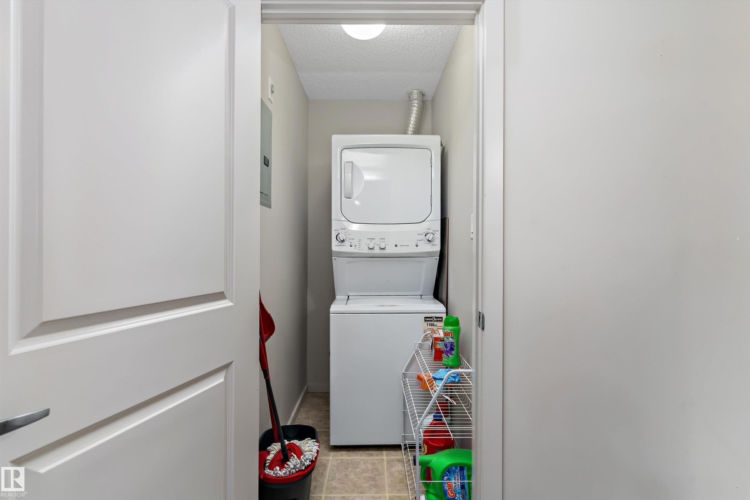 Dedicated laundry closet featuring a stackable washer and dryer unit, tiled flooring, and light neutral wall paint - 231 344 Windermere Road, Edmonton, AB - Indoor Photo Showing Laundry Room