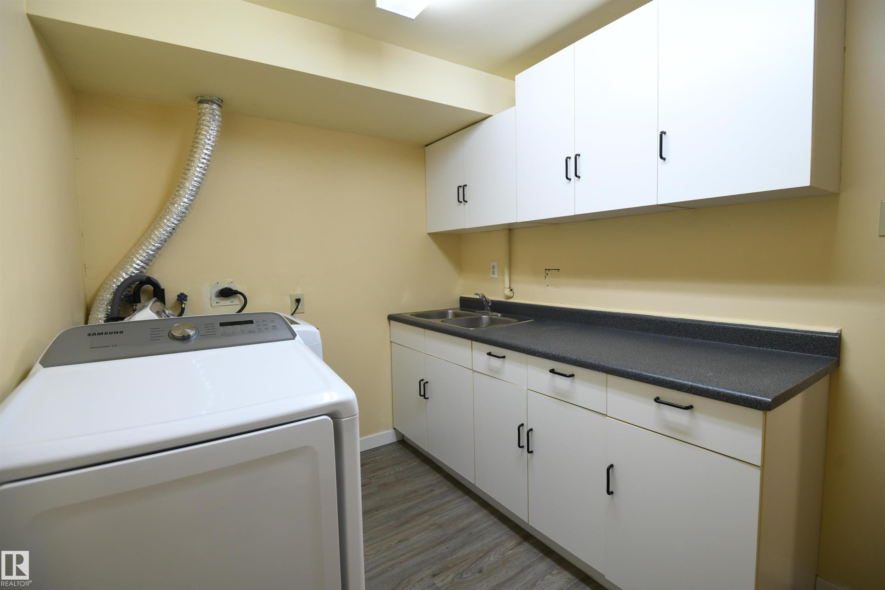 The laundry room is located in the lower level, has some welcome extra floorspace, cabinetry, counter space, and even a double sink - 6706 36A Avenue, Edmonton, AB - Indoor Photo Showing Laundry Room