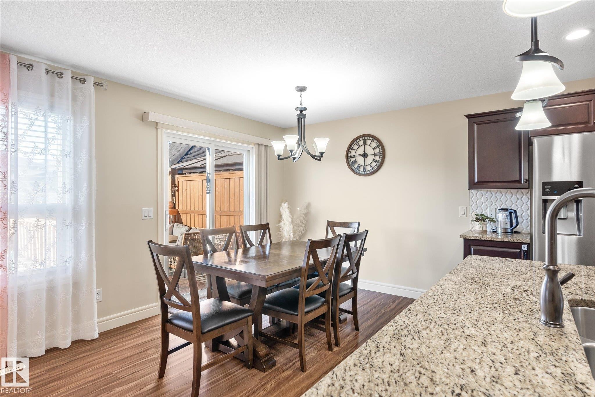 Dining area featuring wood-finish flooring, a contemporary chandelier, and a sliding glass door - 6864 Evans Wynd, Edmonton, AB - Indoor Photo Showing Dining Room