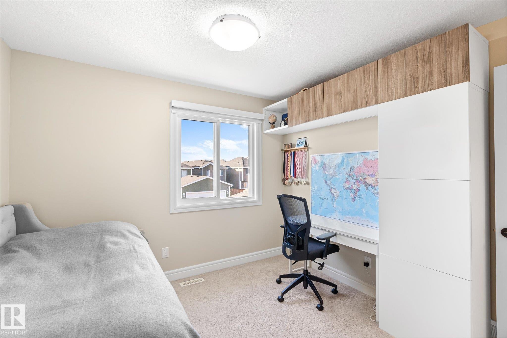 Integrated built-in desk with overhead wood-finish cabinetry, white shelving, and a white window frame - 6864 Evans Wynd, Edmonton, AB - Indoor Photo Showing Bedroom