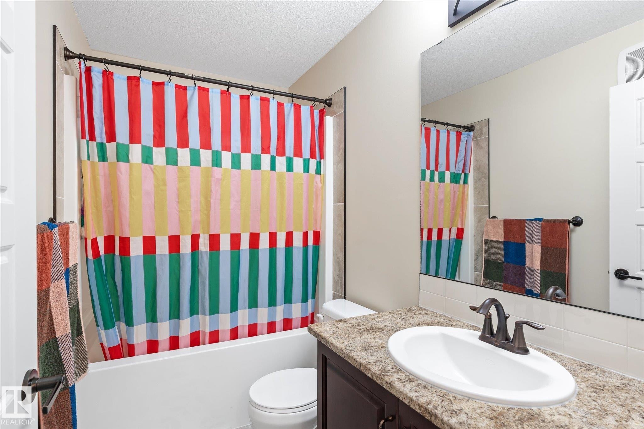Bathroom featuring a built-in tub with a shower fixture, a vanity with a light-toned countertop, an integrated oval sink, and a wall-mounted mirror - 6864 Evans Wynd, Edmonton, AB - Indoor Photo Showing Bathroom