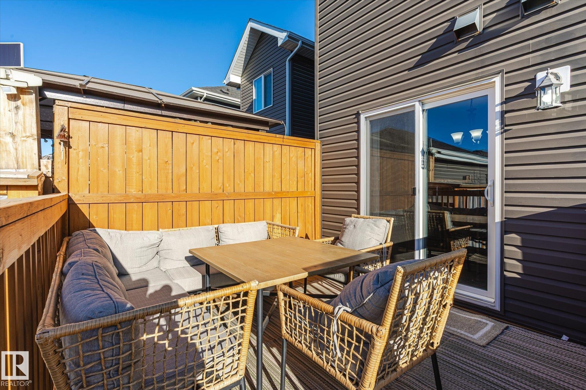 Private deck featuring wood privacy fencing, grey siding exterior, a sliding glass door, and an exterior wall light fixture - 6864 Evans Wynd, Edmonton, AB - Outdoor