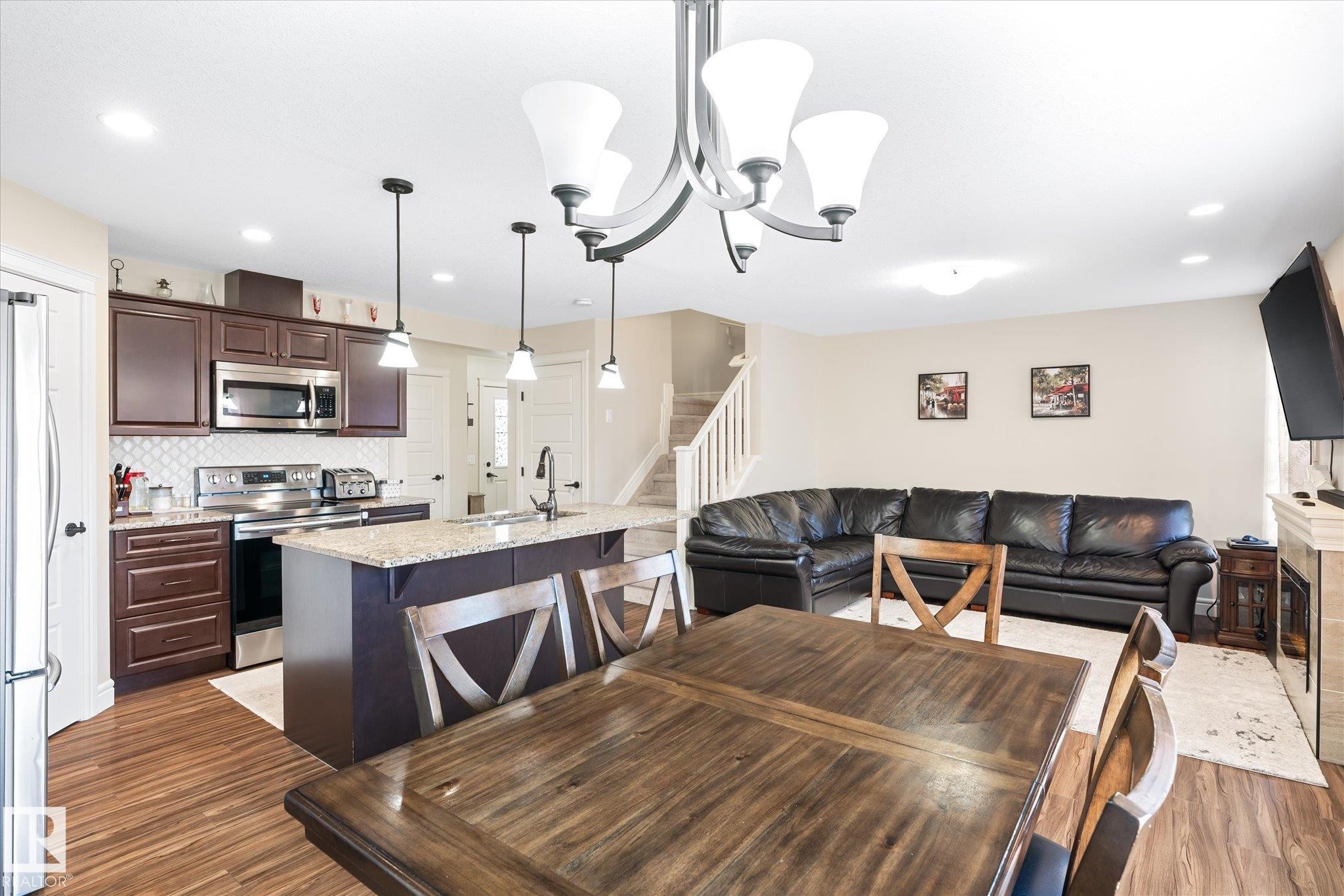 Open-concept living area featuring a kitchen with stainless steel appliances, dark wood cabinetry, and a central island with a sink - 6864 Evans Wynd, Edmonton, AB - Indoor