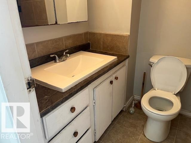 Bathroom featuring a white vanity with integrated sink, chrome faucet, dark countertop, ceramic tile backsplash, and a wall-mounted mirrored medicine cabinet - 6117 120 Avenue, Edmonton, AB - Indoor Photo Showing Bathroom