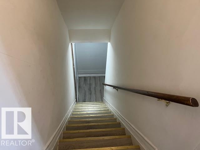Stairwell featuring a dark wood handrail, white painted walls, and wood-finish stair treads with brass-toned strips - 6117 120 Avenue, Edmonton, AB - Indoor Photo Showing Other Room