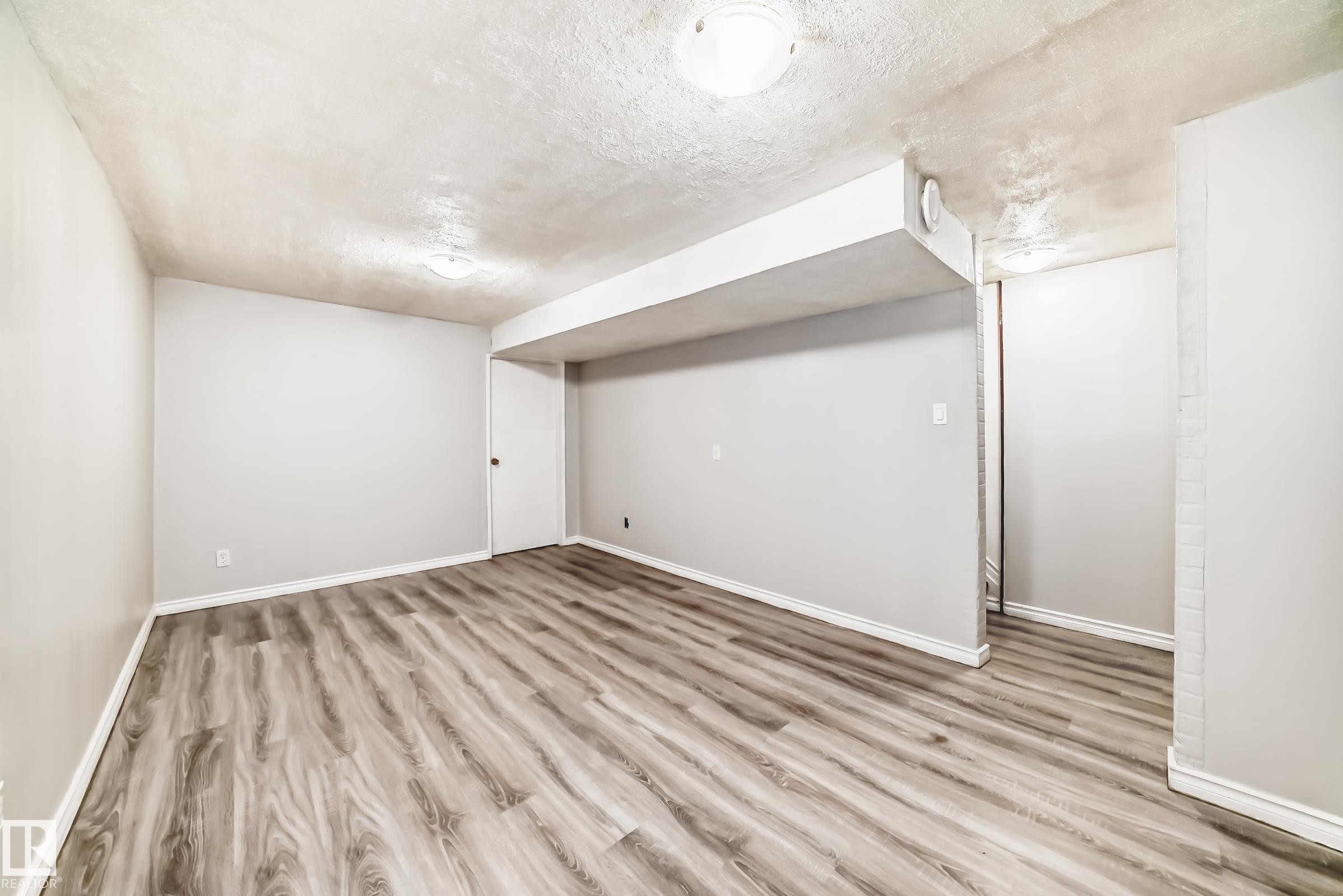 Spacious room featuring wood-finish flooring, light grey walls, white trim, and overhead lighting - 6117 120 Avenue, Edmonton, AB - Indoor Photo Showing Other Room