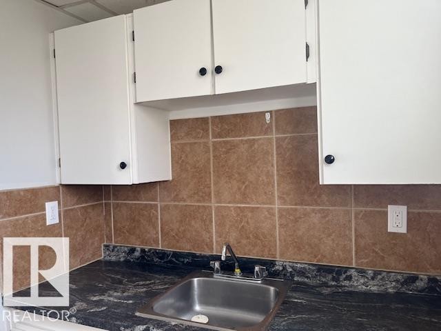 Kitchen area featuring white upper cabinetry, a stainless steel sink, a dark patterned countertop, and a brown tiled backsplash - 6117 120 Avenue, Edmonton, AB - Indoor Photo Showing Kitchen