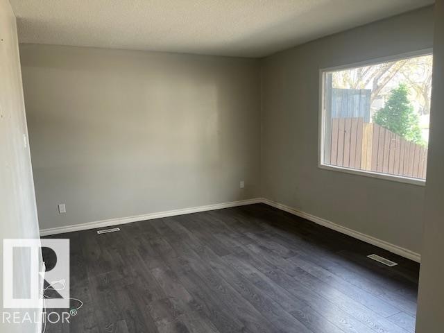 Spacious room featuring neutral painted walls, wood-finish flooring, and white baseboards - 6117 120 Avenue, Edmonton, AB - Indoor Photo Showing Other Room