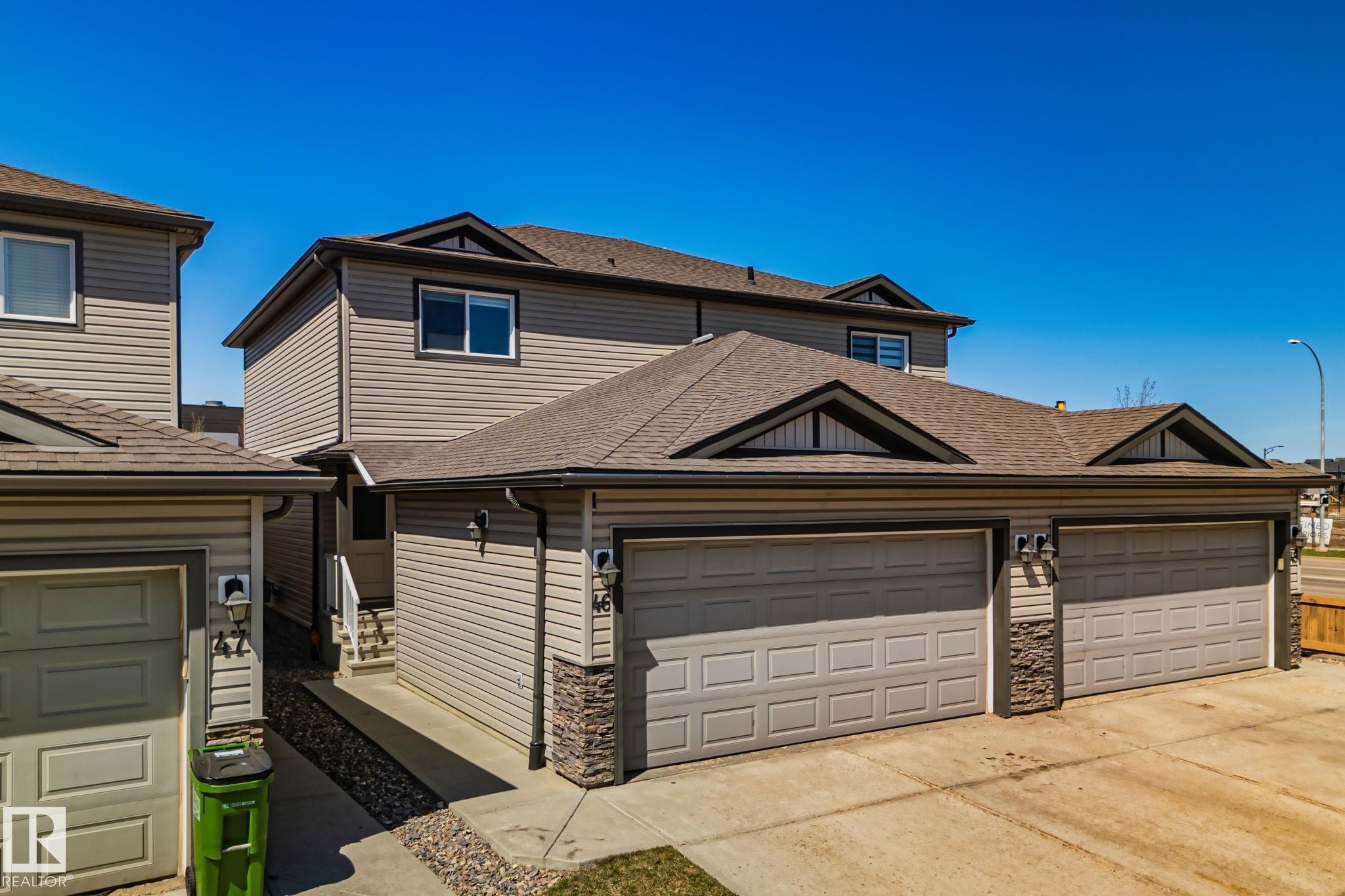 Exterior featuring light grey horizontal siding, stone veneer accents, multiple dormer windows, and a brown shingle roof - 46 445 Brintnell Boulevard, Edmonton, AB - Outdoor