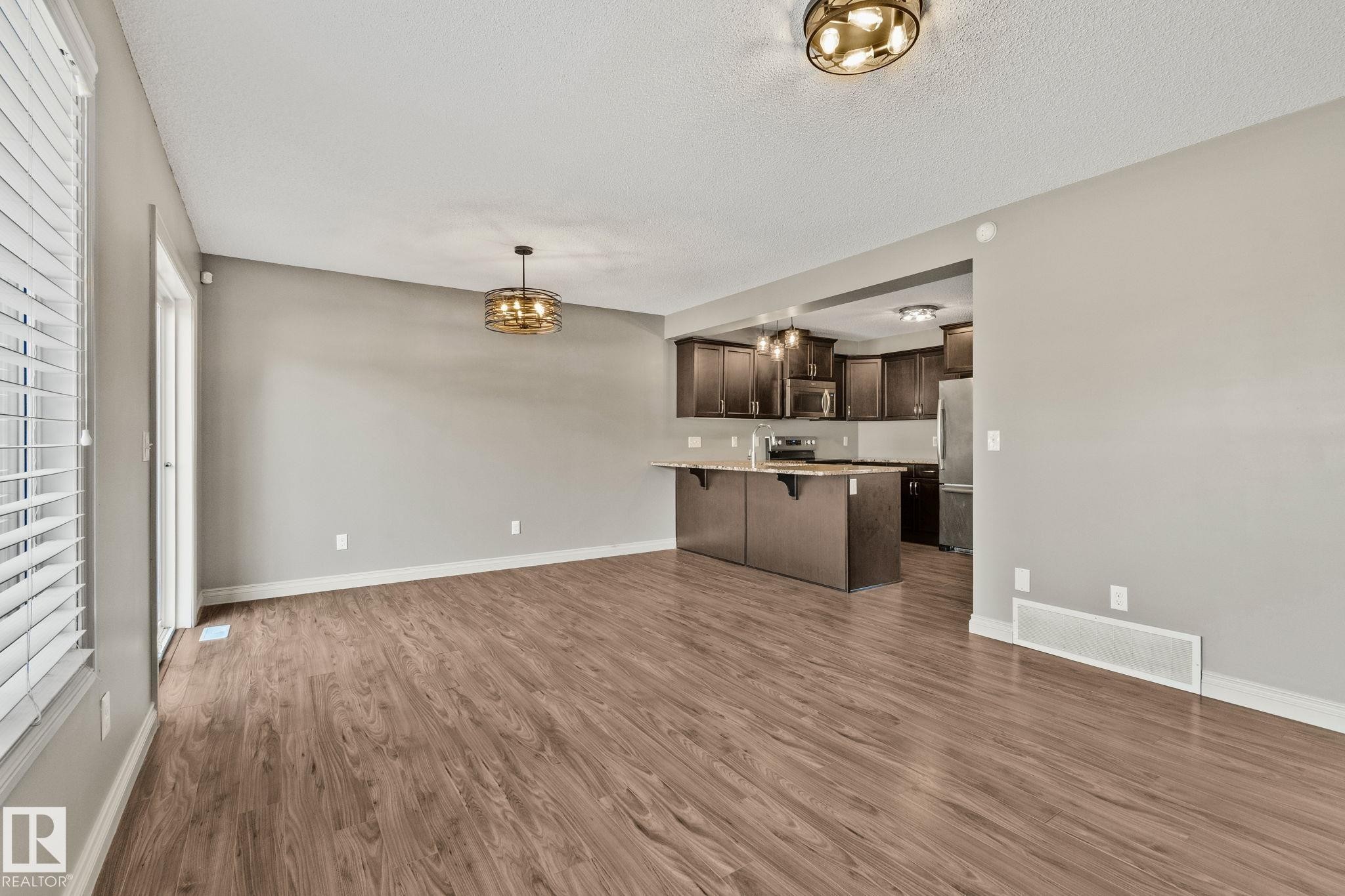 Expansive main living area featuring wood-finish flooring, a contemporary chandelier, and a sliding glass door - 46 445 Brintnell Boulevard, Edmonton, AB - Indoor Photo Showing Kitchen