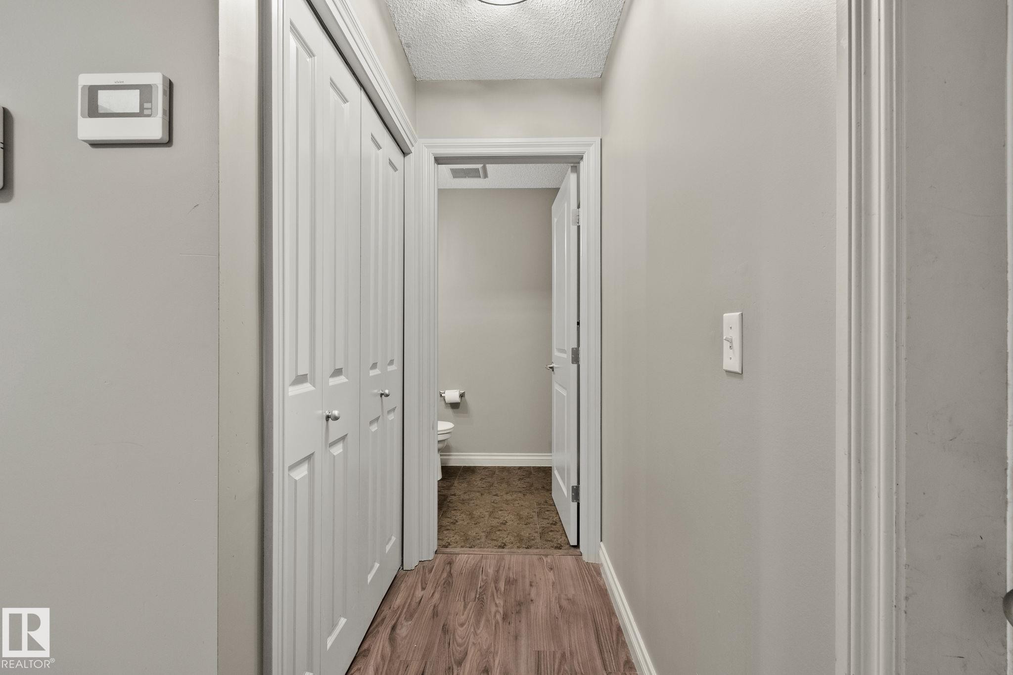 Hallway featuring wood-finish flooring, light grey painted walls, and white bi-fold closet doors - 46 445 Brintnell Boulevard, Edmonton, AB - Indoor Photo Showing Other Room