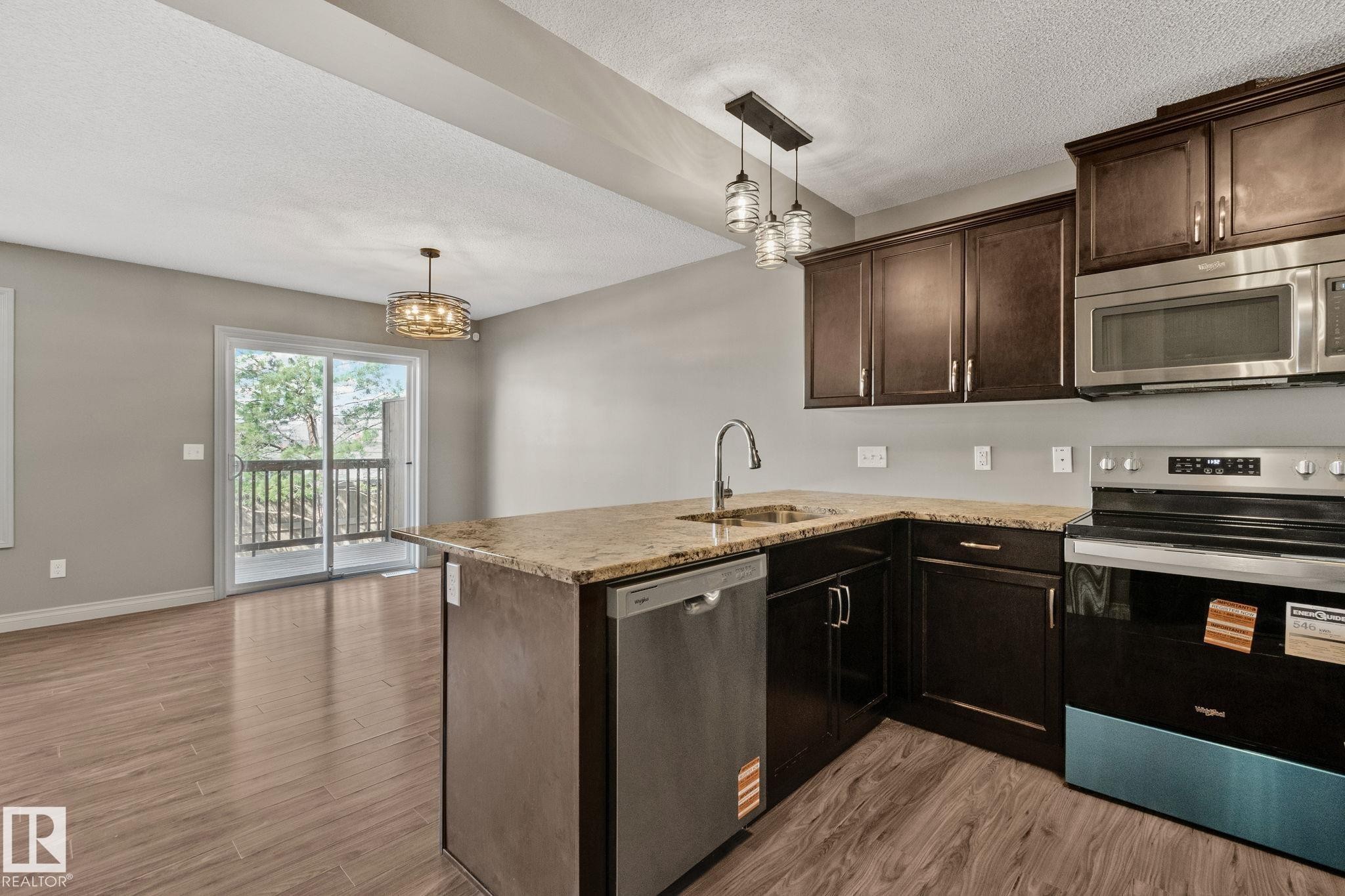 Kitchen island featuring a single-basin sink with a gooseneck faucet, dark wood cabinetry, and a light-colored countertop - 46 445 Brintnell Boulevard, Edmonton, AB - Indoor Photo Showing Kitchen With Stainless Steel Kitchen
