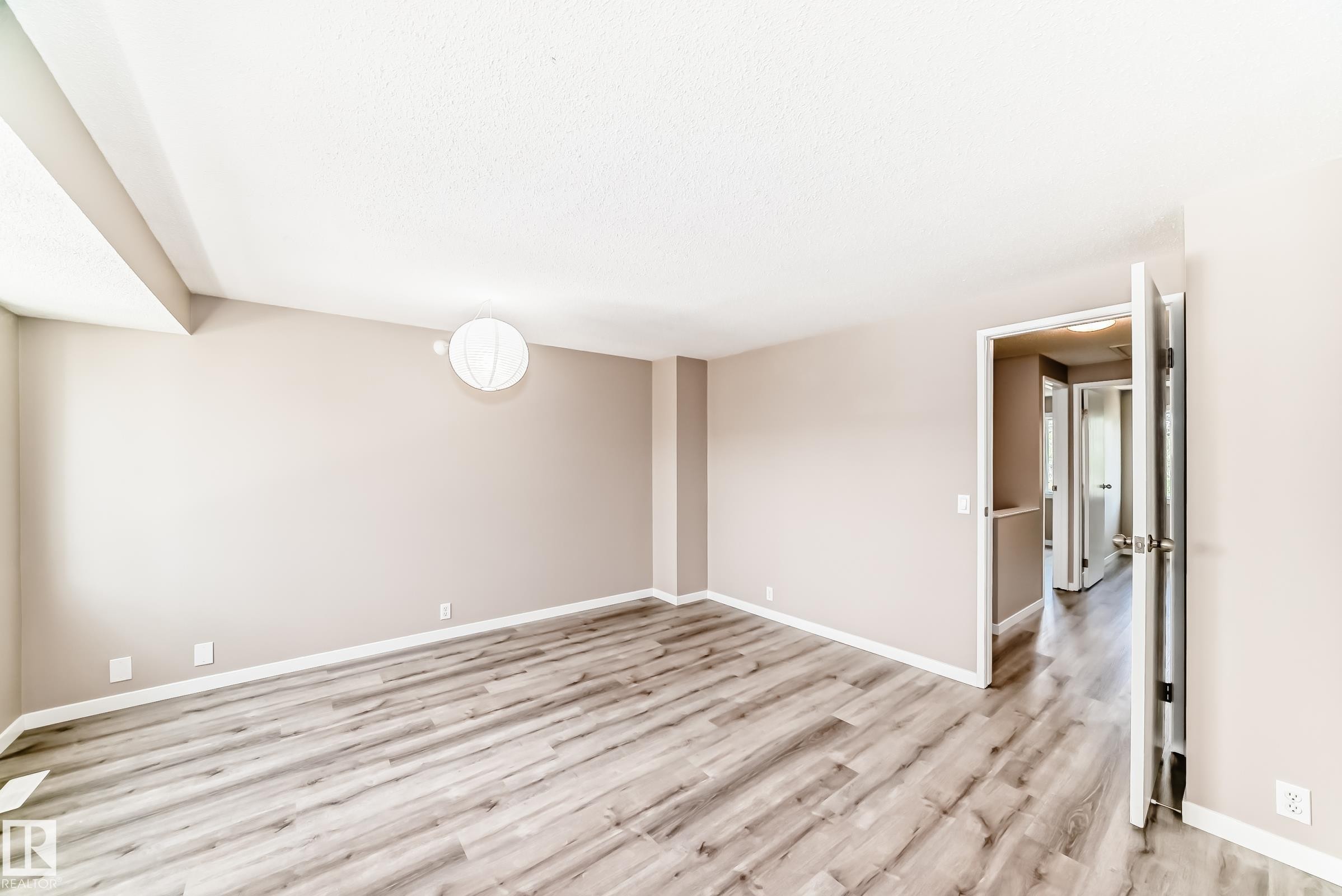 Spacious room featuring wood-finish flooring, light neutral wall paint, white baseboards, and a contemporary wall-mounted light fixture - 2578 138A Avenue, Edmonton, AB - Indoor Photo Showing Other Room