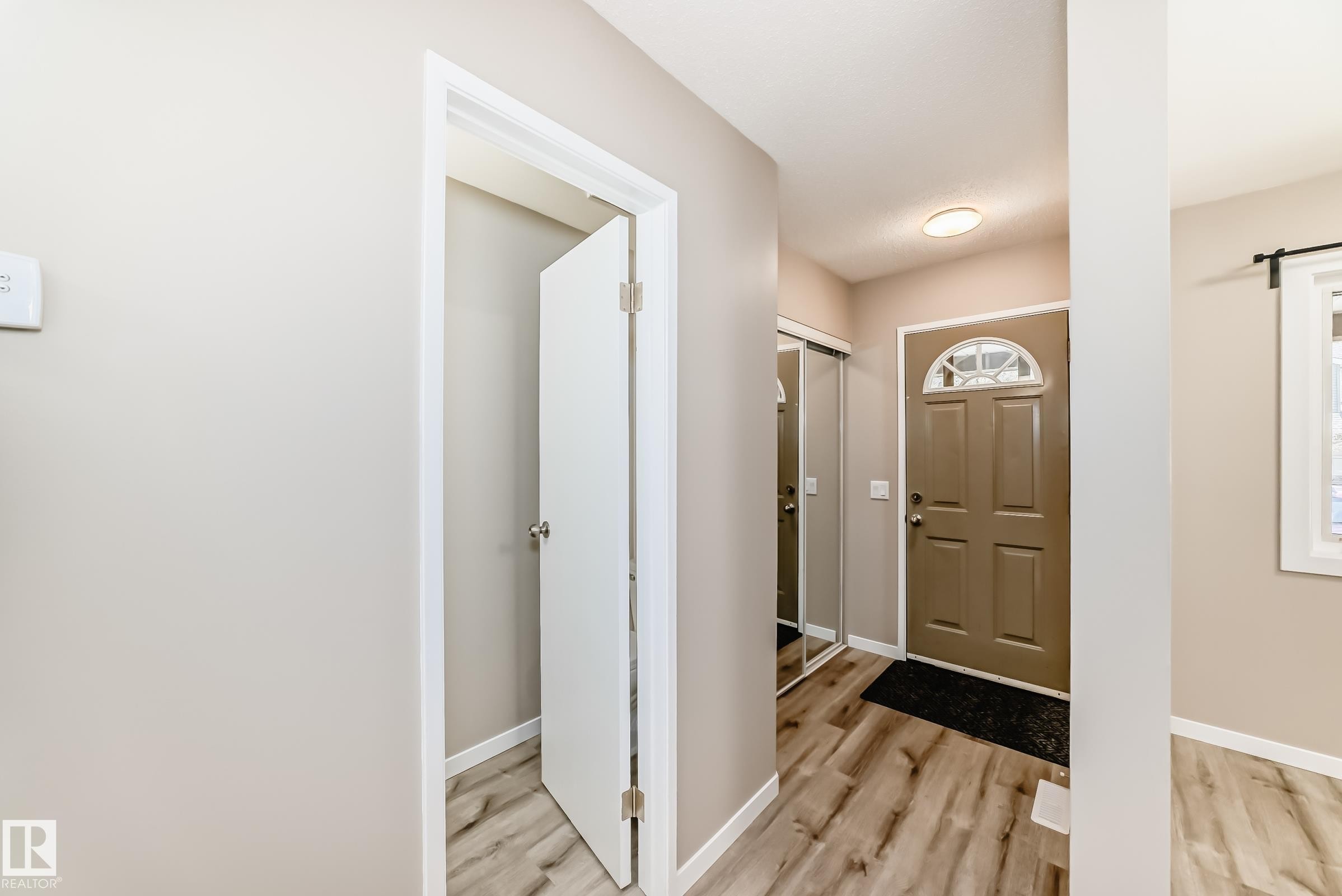Entryway featuring wood-finish flooring, a paneled front door with an arched transom, and a mirrored sliding closet door - 2578 138A Avenue, Edmonton, AB - Indoor Photo Showing Other Room