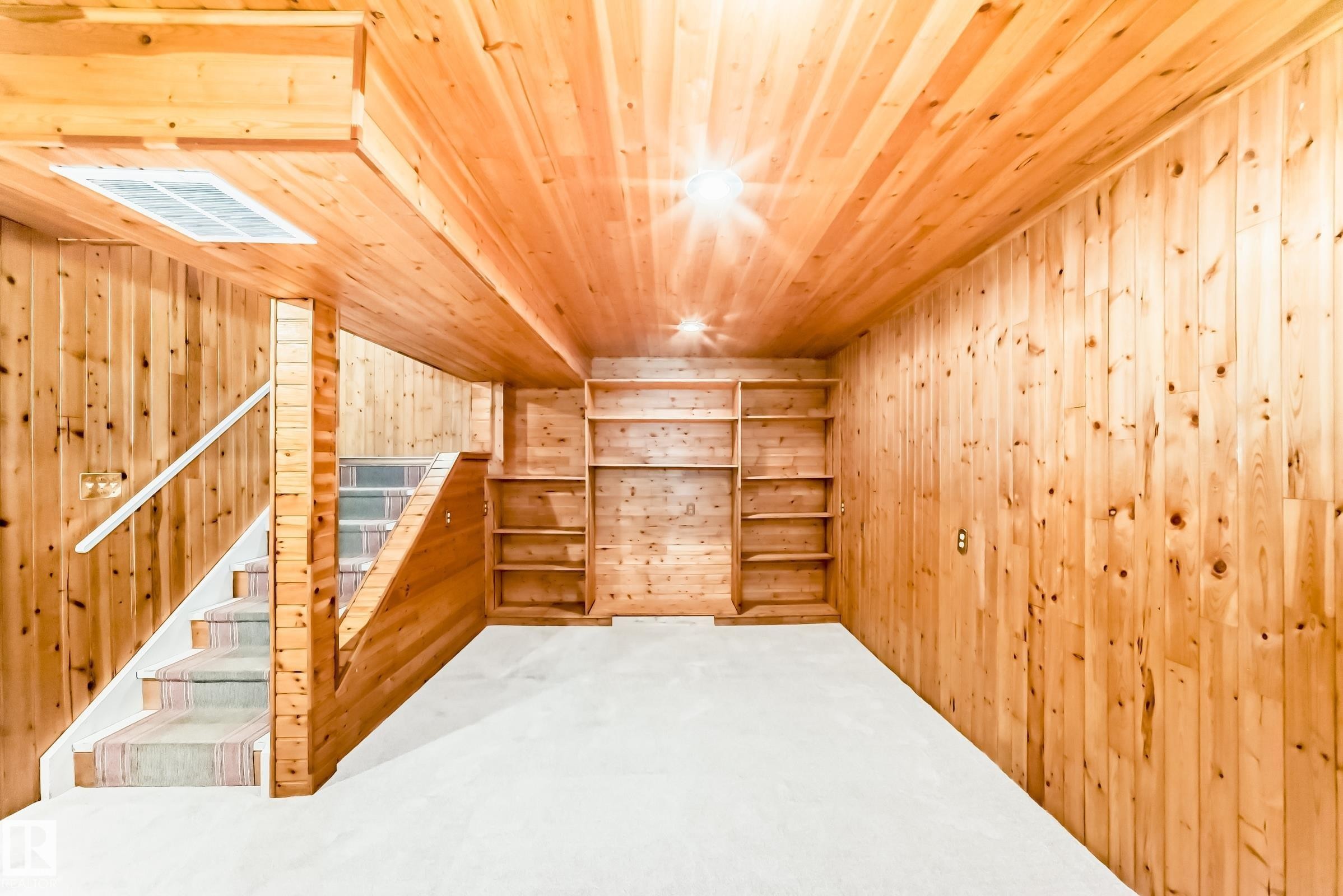 Carpeted room featuring wood-paneled walls and ceiling, built-in shelving, and a carpeted staircase with a white handrail - 2578 138A Avenue, Edmonton, AB - Indoor Photo Showing Other Room