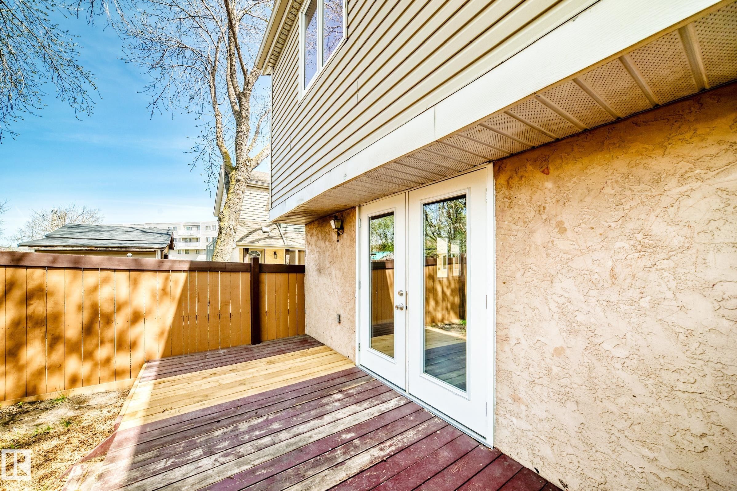 Outdoor wood deck with a privacy fence, textured stucco exterior, and white frame double doors - 2578 138A Avenue, Edmonton, AB - Outdoor