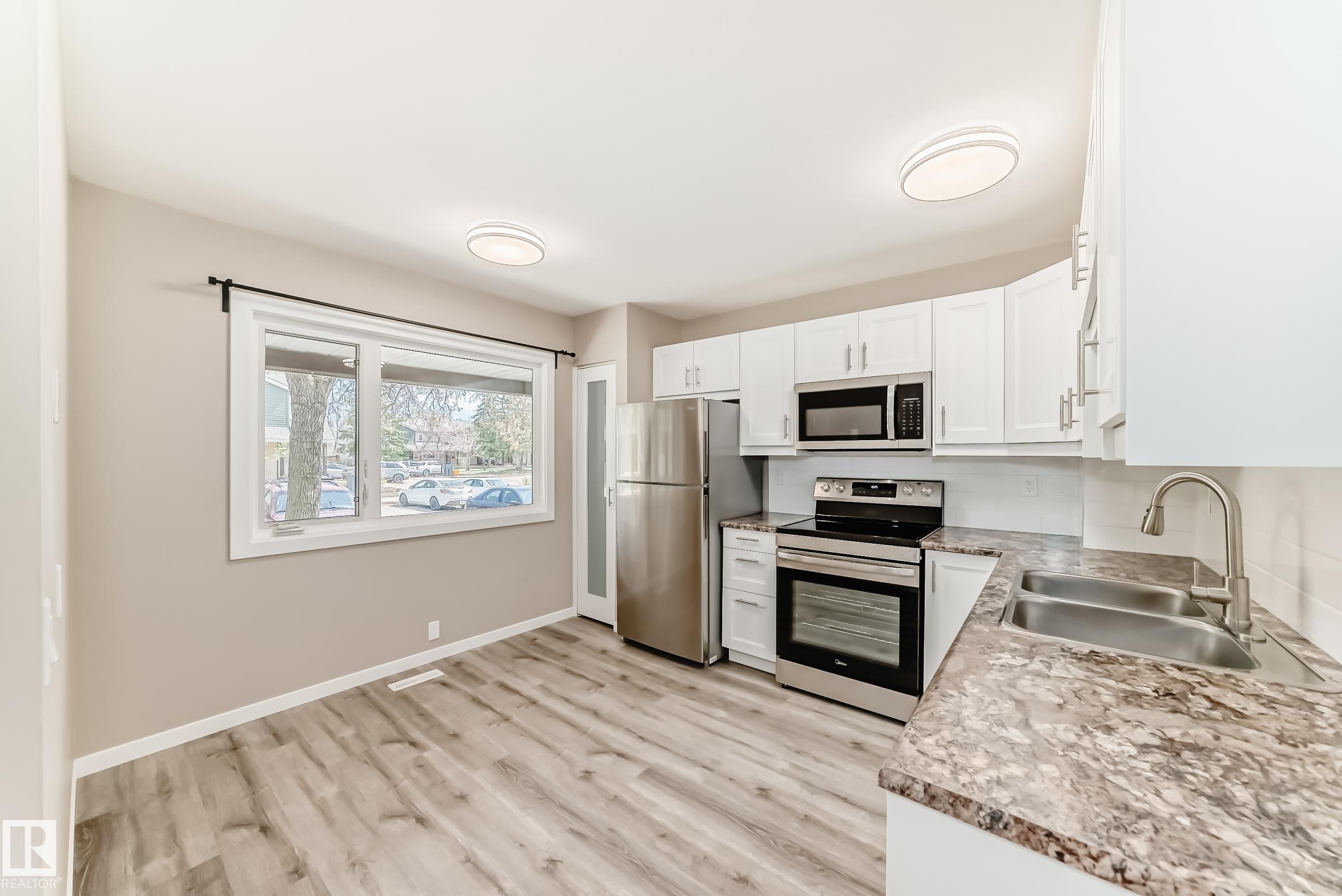 Modern kitchen featuring white cabinetry, stainless steel appliances, wood-finish flooring, and a double basin sink - 2578 138A Avenue, Edmonton, AB - Indoor Photo Showing Kitchen With Double Sink