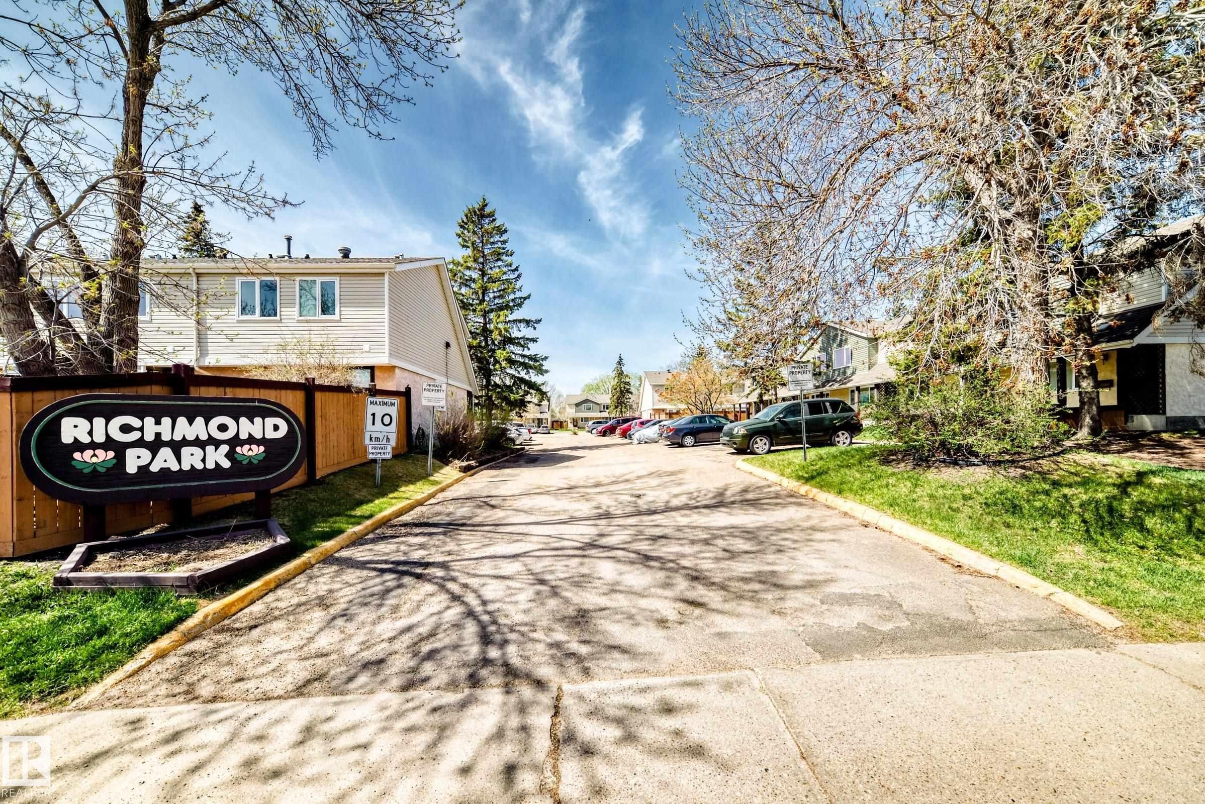 Paved community entrance with a prominent "Richmond Park" sign, bordered by mature trees and manicured lawns - 2578 138A Avenue, Edmonton, AB - Outdoor