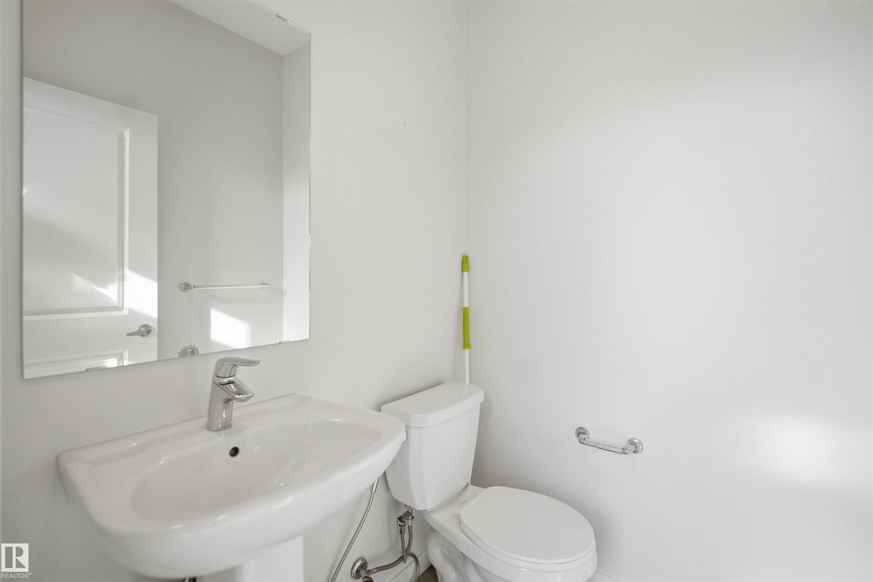 Bathroom featuring a white pedestal sink with a chrome faucet, a wall-mounted mirror, and a white toilet - 2125 Maple Road Nw, Edmonton, AB - Indoor Photo Showing Bathroom