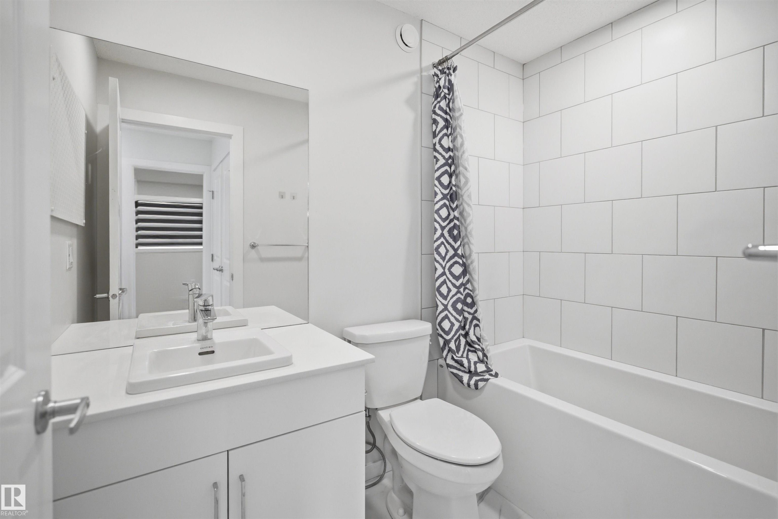 Well-appointed bathroom featuring a vanity with an integrated sink, a large mirror, a toilet, and a bathtub with white subway tile surround - 2125 Maple Road Nw, Edmonton, AB - Indoor Photo Showing Bathroom