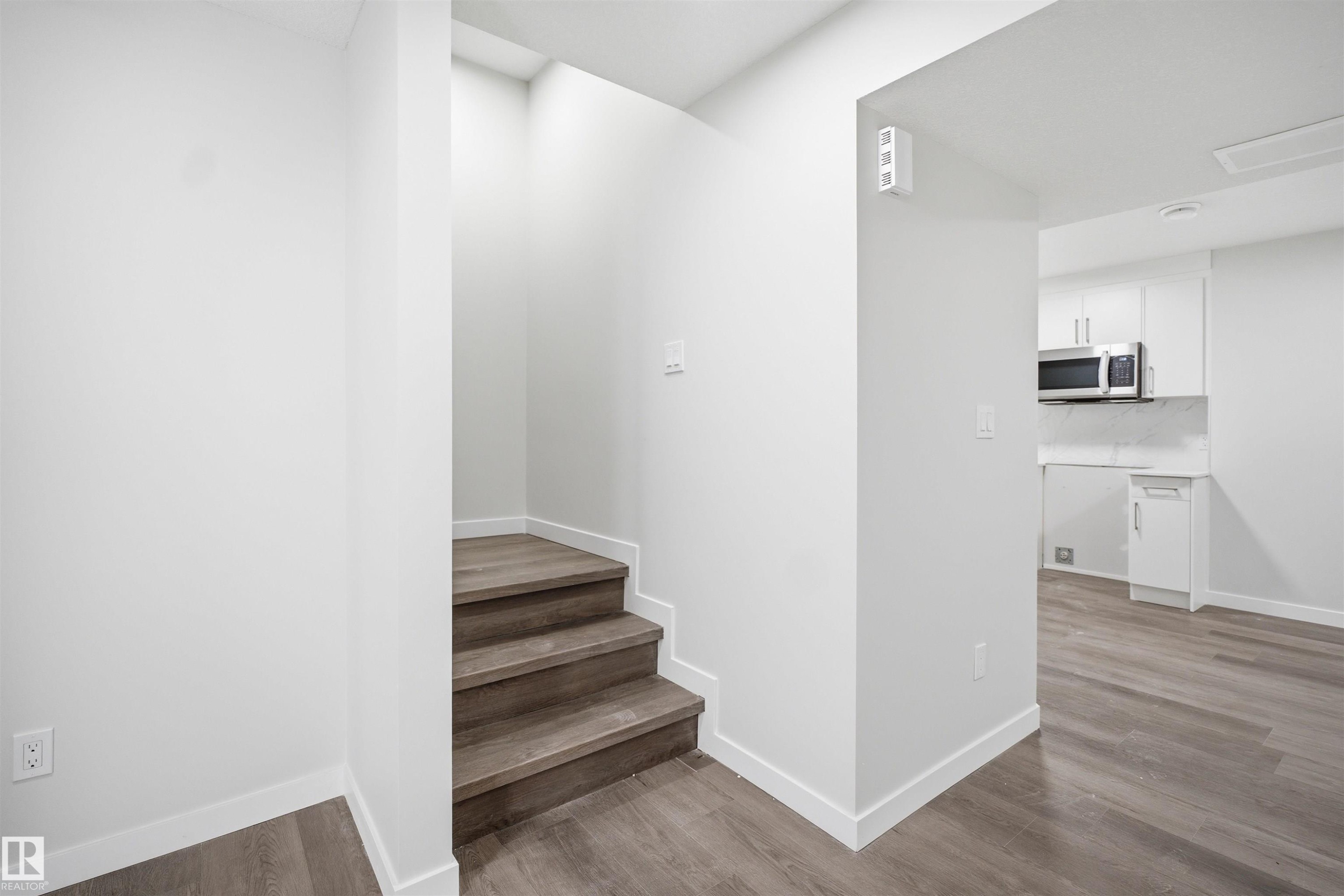 The property features a staircase with wood-look treads and white risers, leading to an upper level - 2125 Maple Road Nw, Edmonton, AB - Indoor Photo Showing Other Room