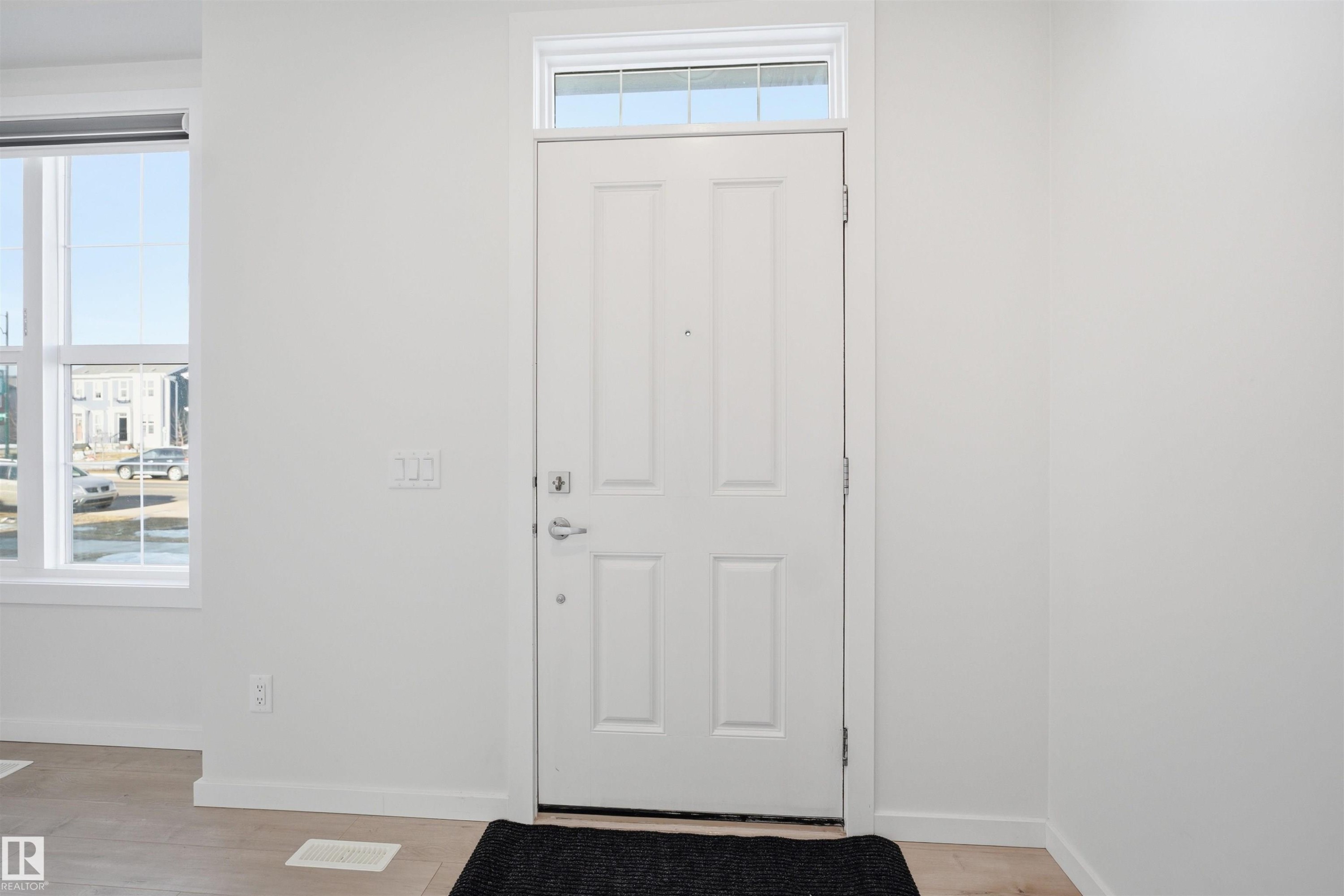 Entryway featuring a white paneled door with a transom window above, a large window providing natural light, and light-colored flooring - 2125 Maple Road Nw, Edmonton, AB - Indoor Photo Showing Other Room